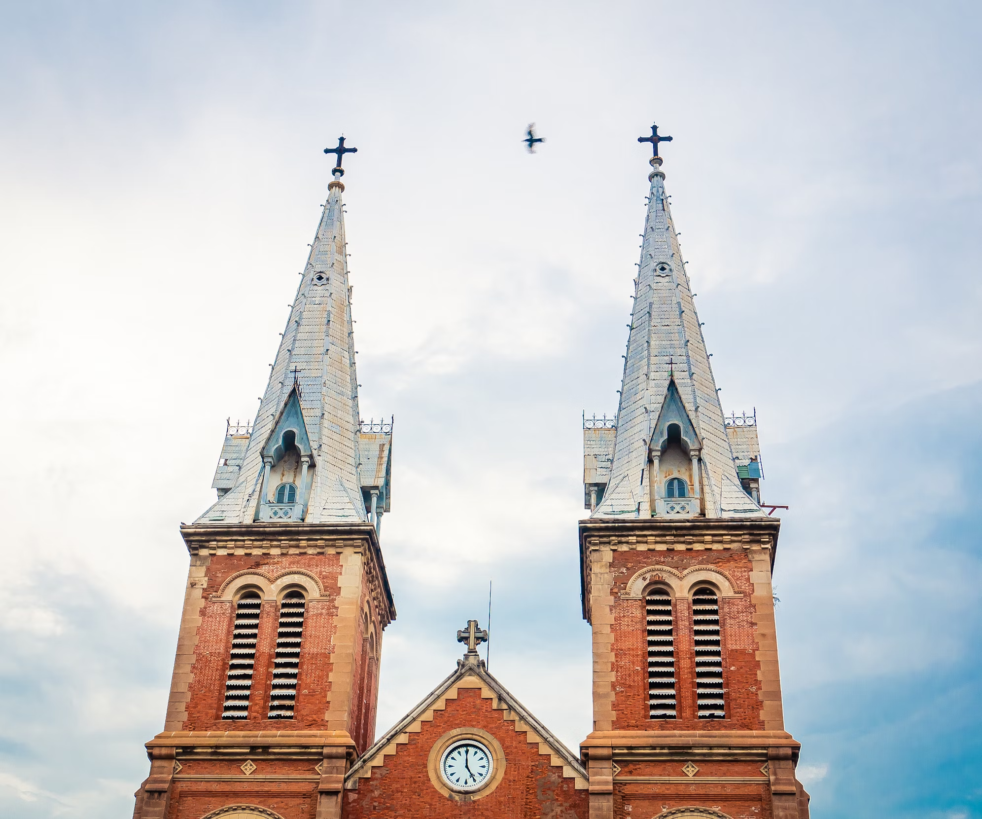 Notre-Dame Cathedral of Saigon with twin bell towers against a cloudy sky