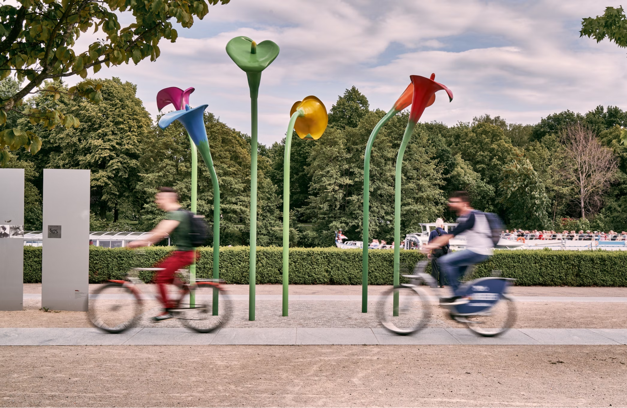 Cyclists ride past modern flower sculptures in a Berlin park