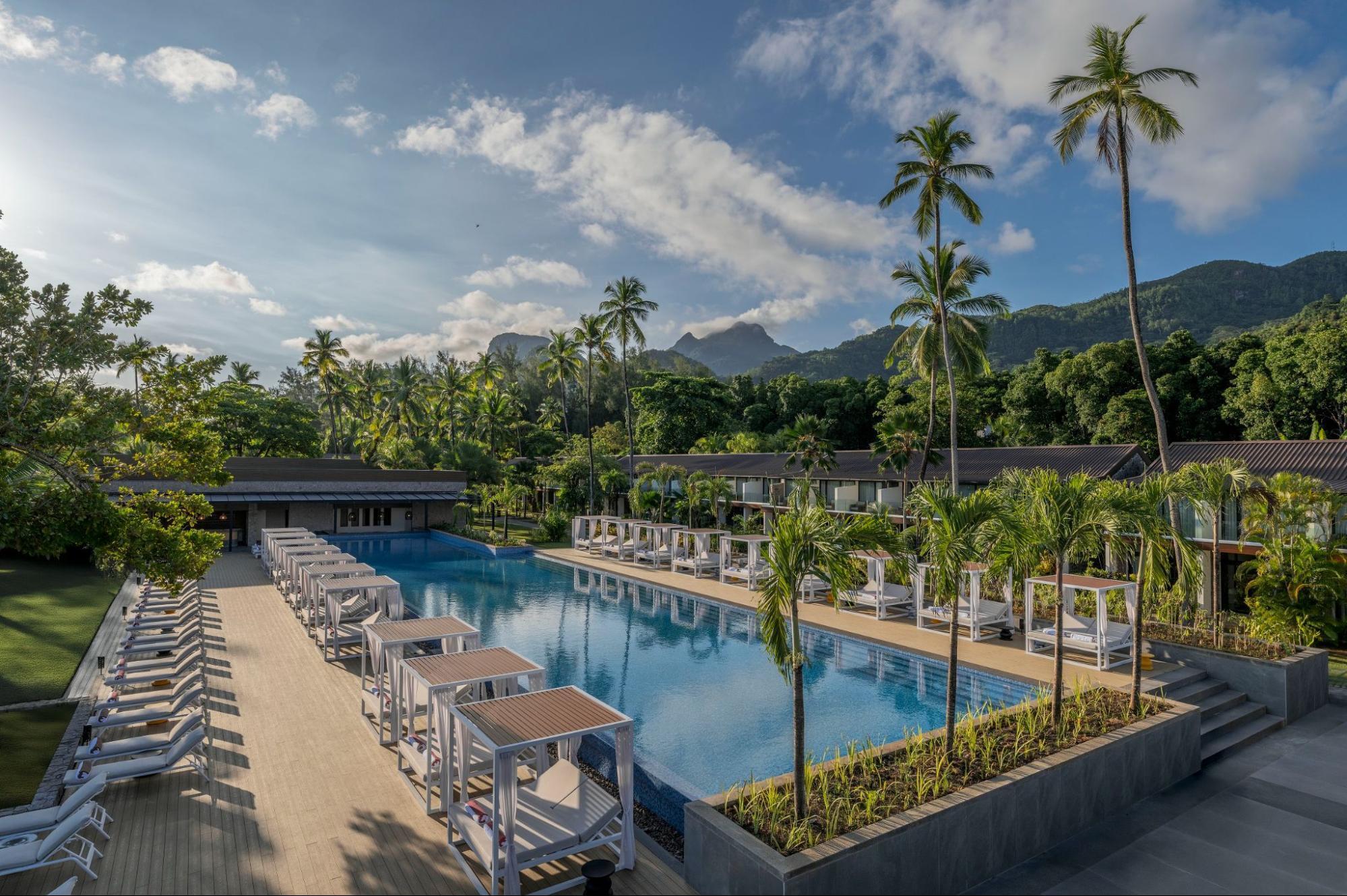 Outdoor pool area at Avani+ Barbarons with mountain backdrop and palm trees