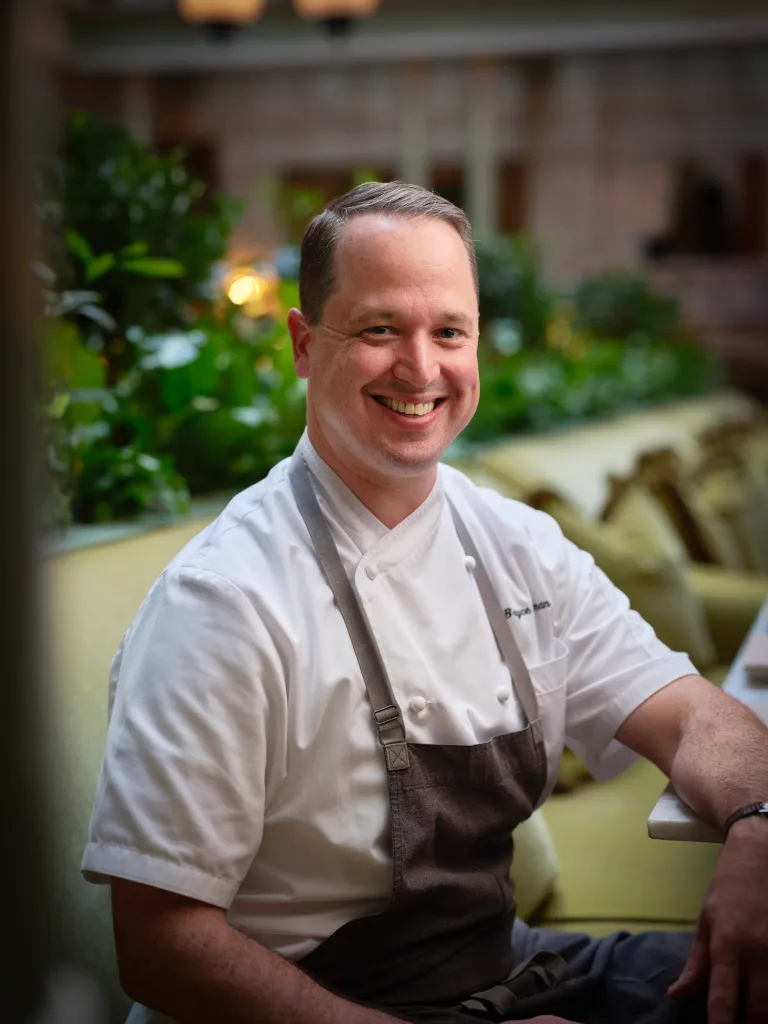Chef Bryce in white uniform smiling at restaurant table