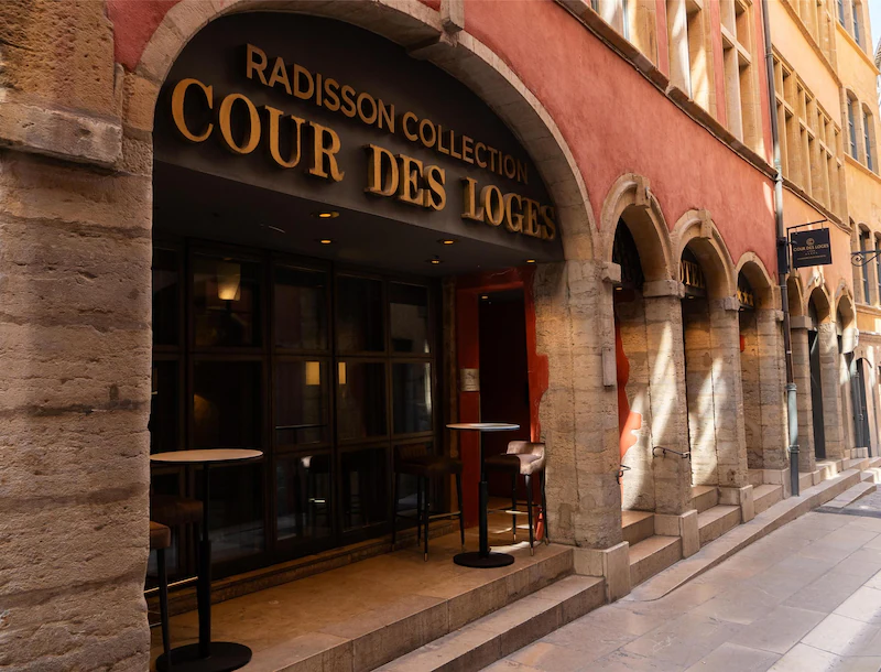 Entrance of Cour des Loges hotel with stone arches and Radisson Collection signage