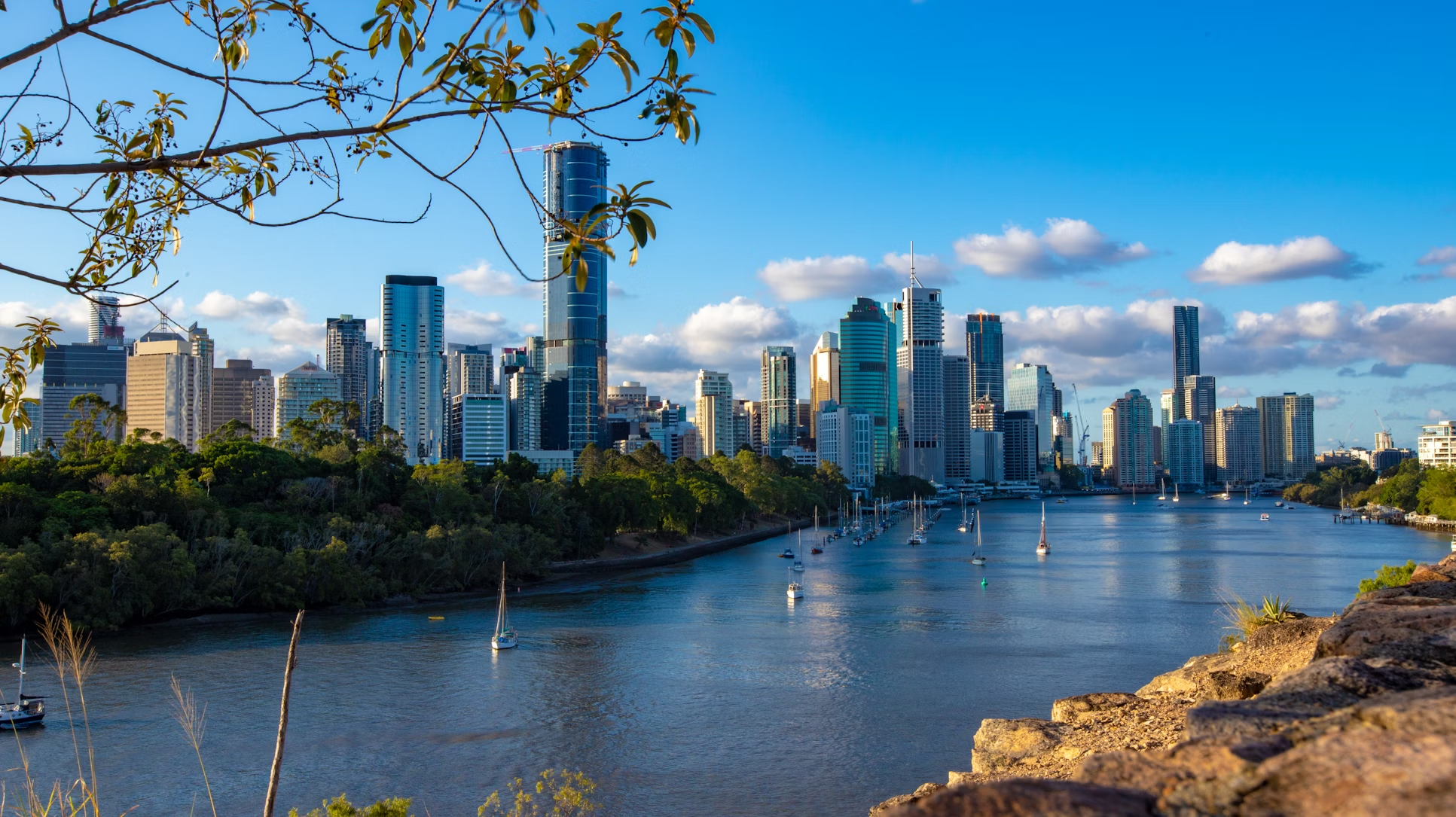 View of Brisbane River with modern city skyline and boats on the water under a blue sky