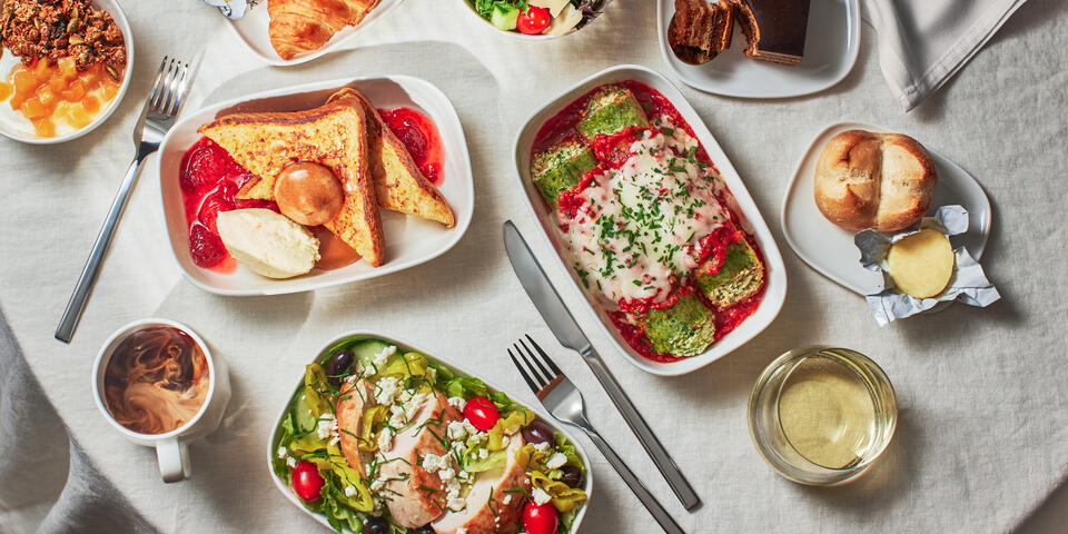 A selection of airline meals including pasta, salad, French toast, dessert, and drinks served on a tray