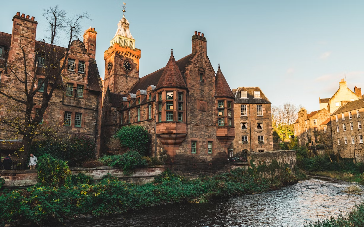 Historic stone buildings along a river in Dean Village, Edinburgh, during golden hour