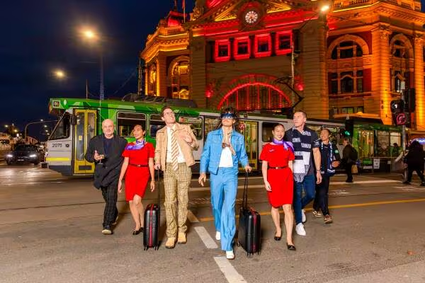 A group of people, including Virgin Australia crew, walking with luggage outside Flinders Street Station at night