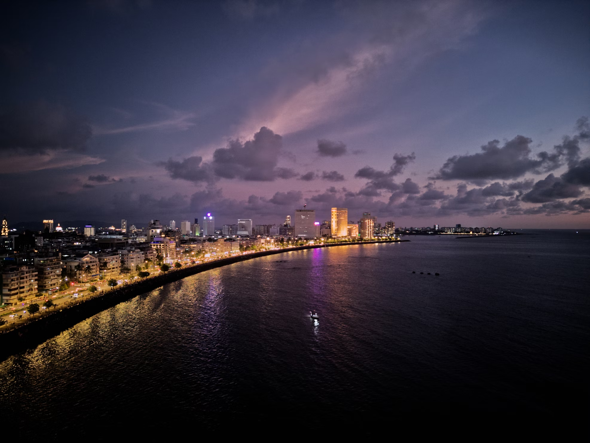 Evening view of Marine Drive coastline in Mumbai with city lights and cloudy sky