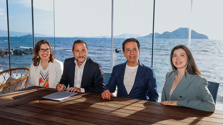 Four people seated at a table by the sea during a signing ceremony