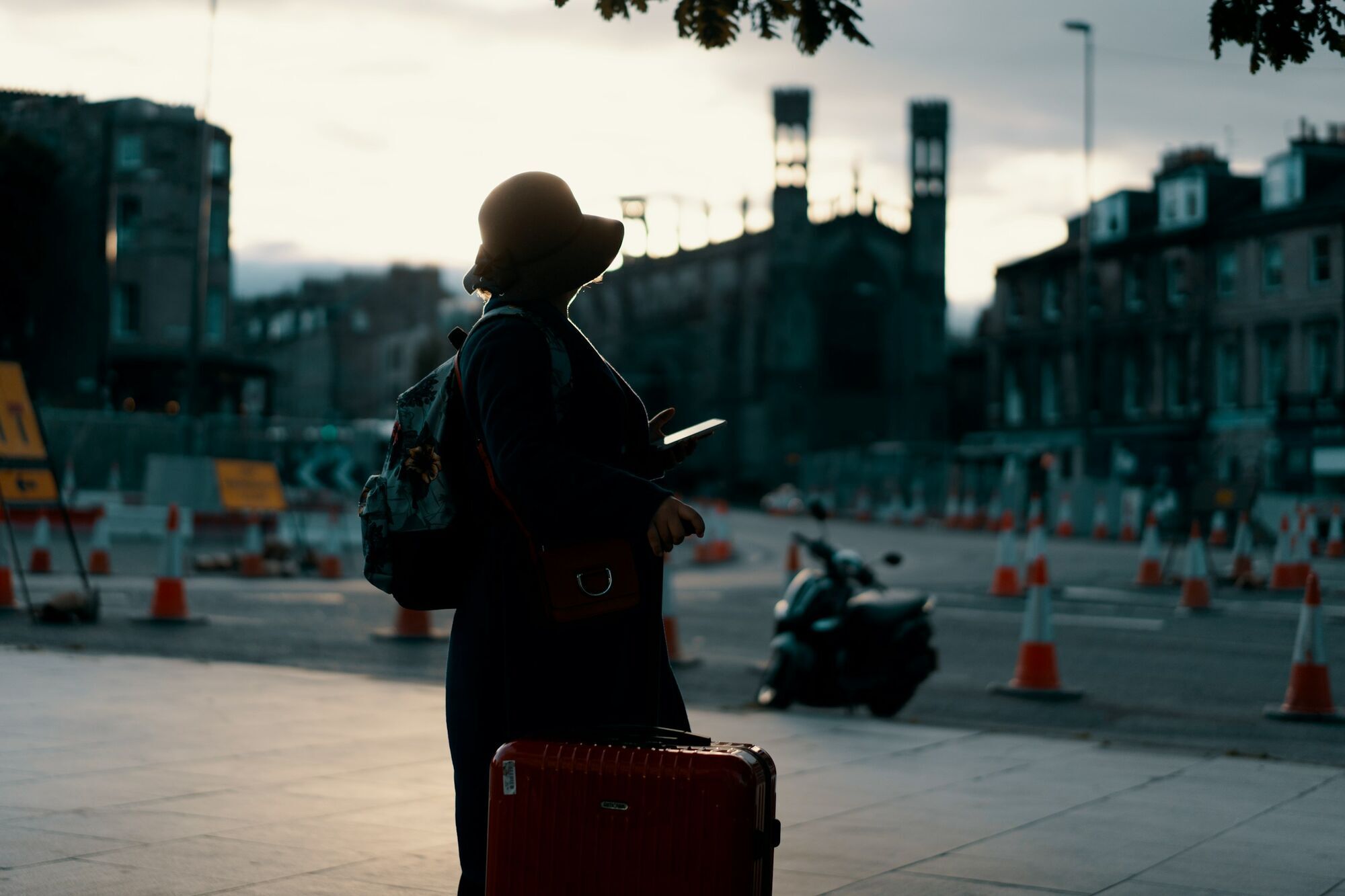 Traveler with suitcase using phone in city street at sunset