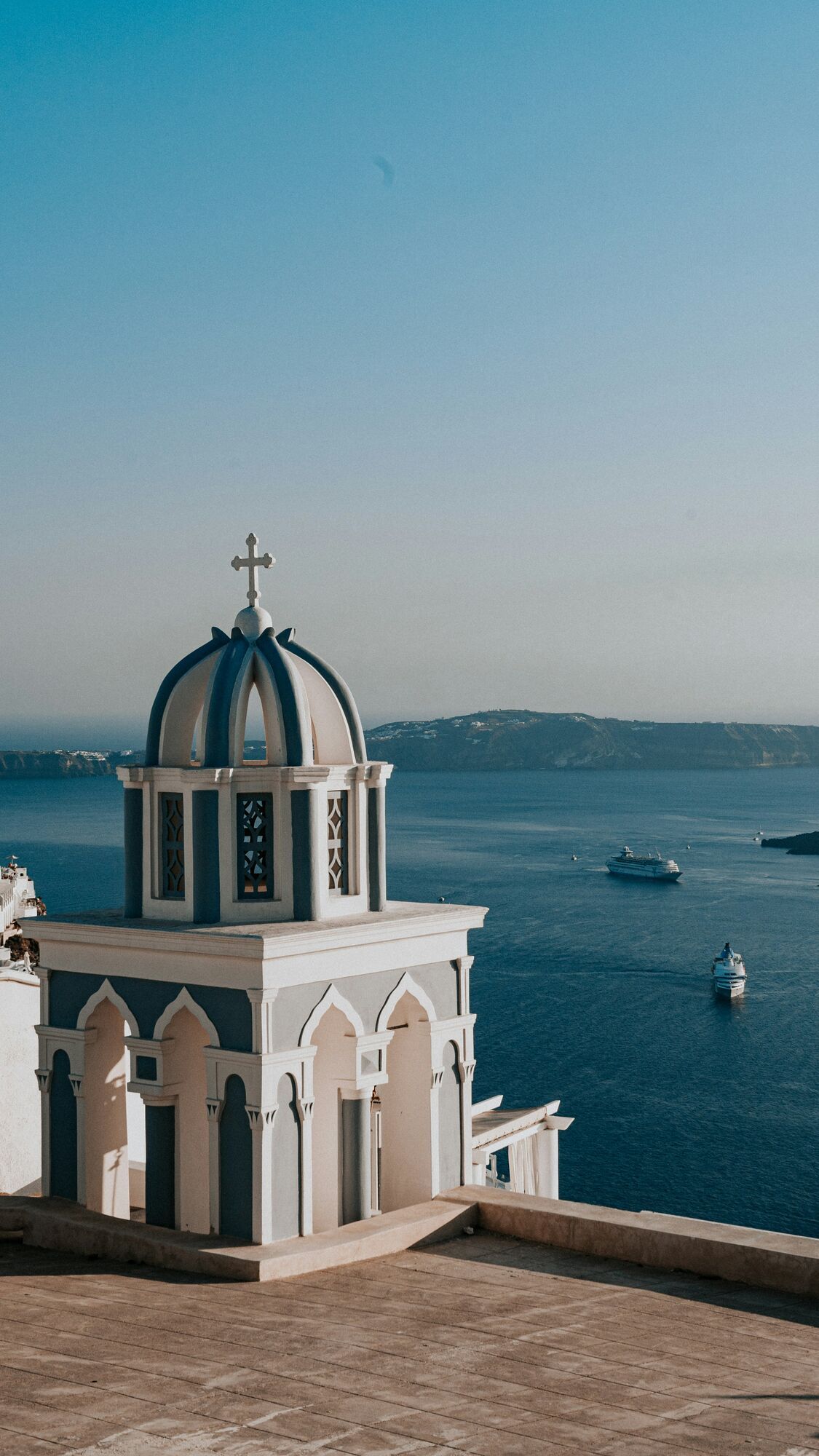 White and blue domed church overlooking the Aegean Sea with cruise ships in the distance