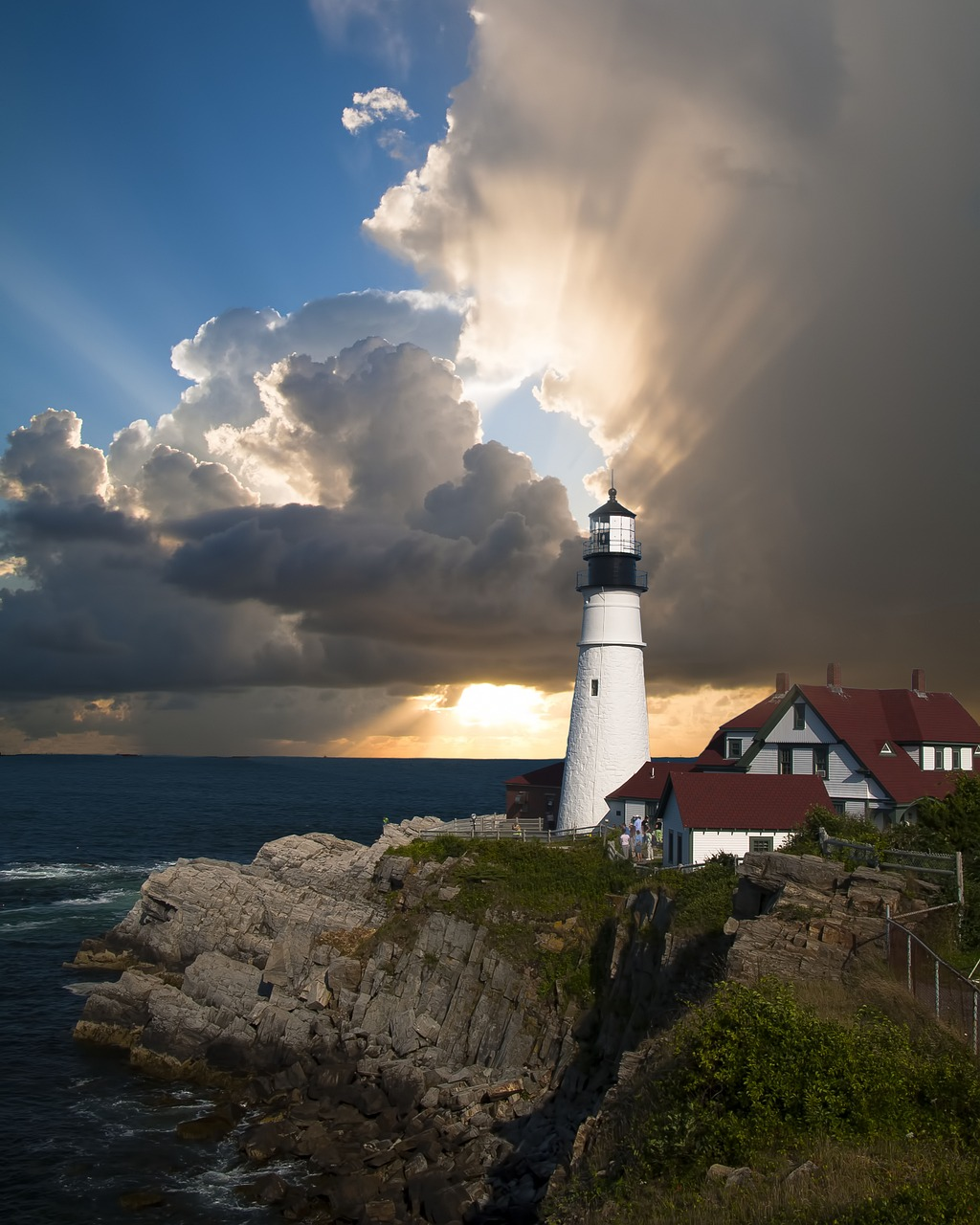 Lighthouse on rocky Portland, Maine coastline at sunset with dramatic clouds