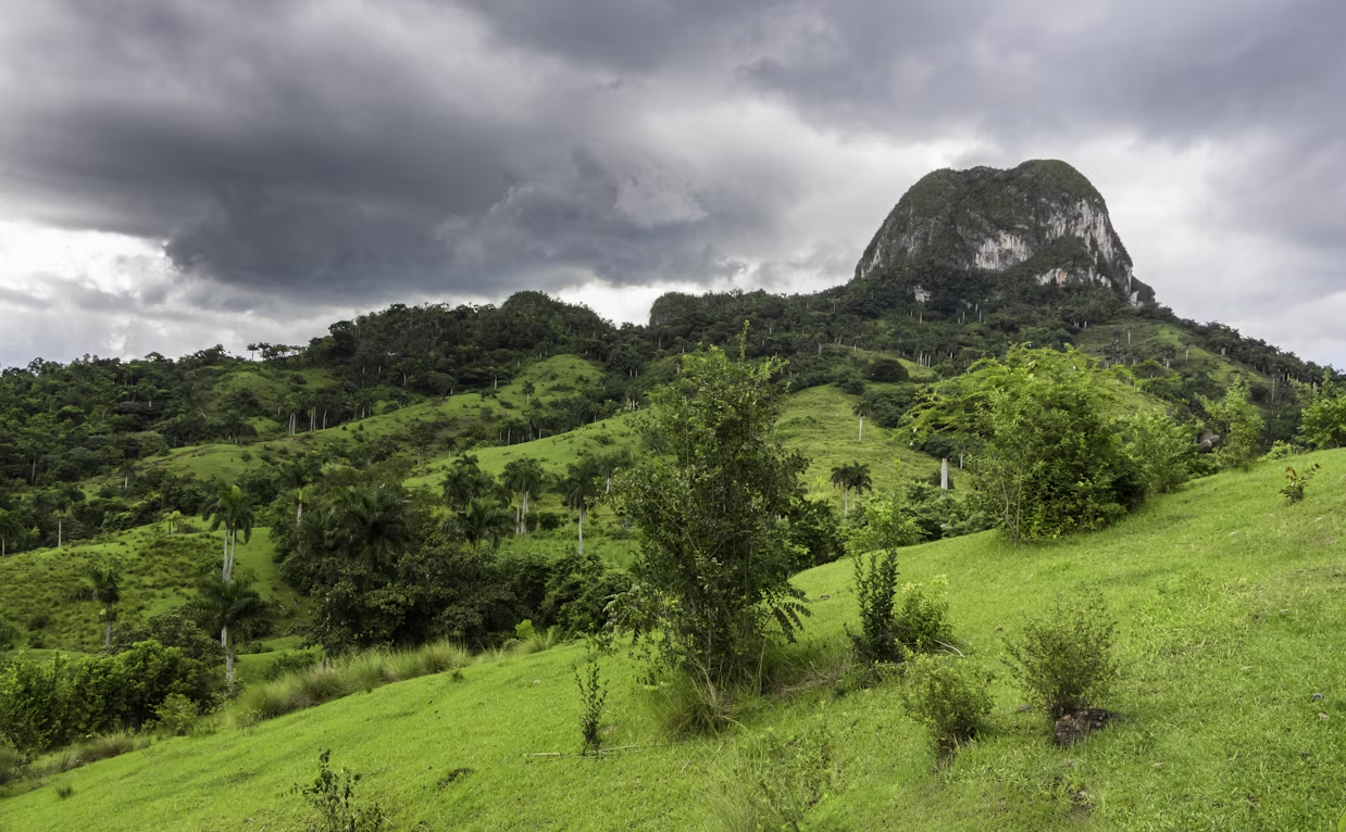 Lush green hills and a rocky mogote in Viñales Valley, Cuba under cloudy skies