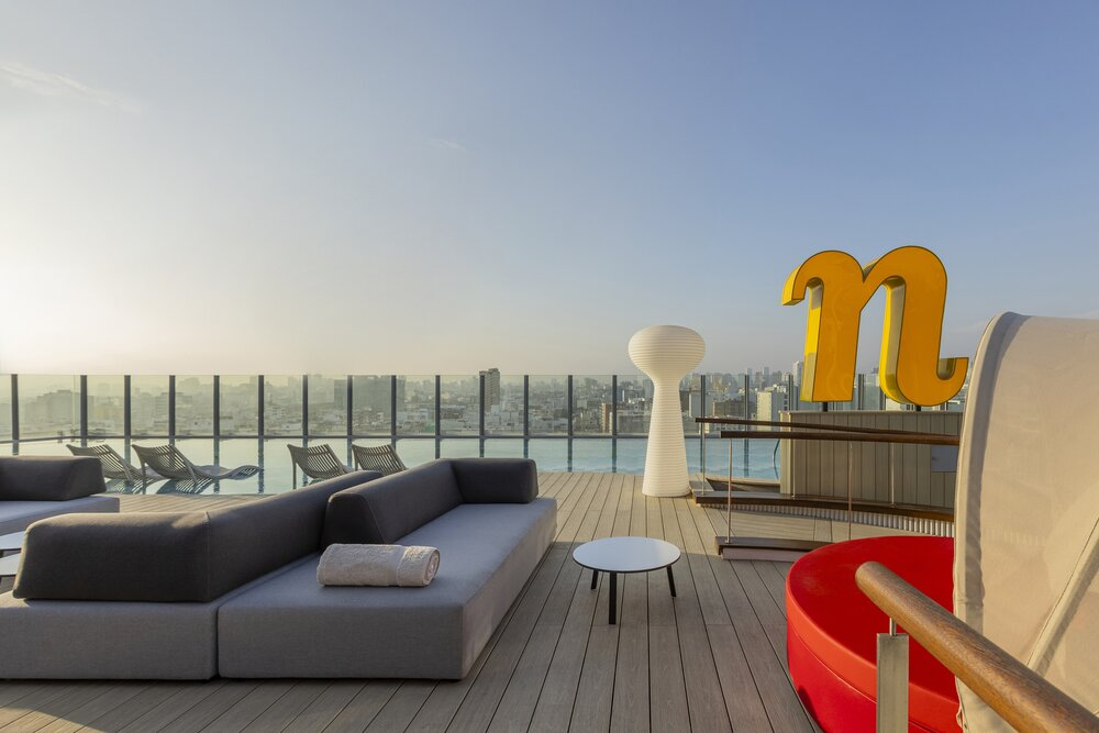 Rooftop lounge with seating, pool, and city skyline view at sunset