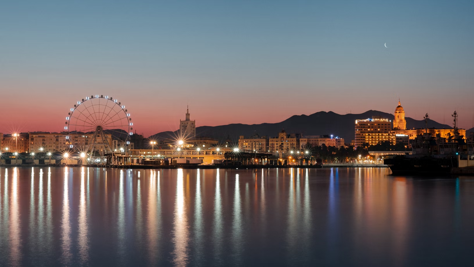 Evening view of Malaga waterfront with illuminated ferris wheel and city skyline