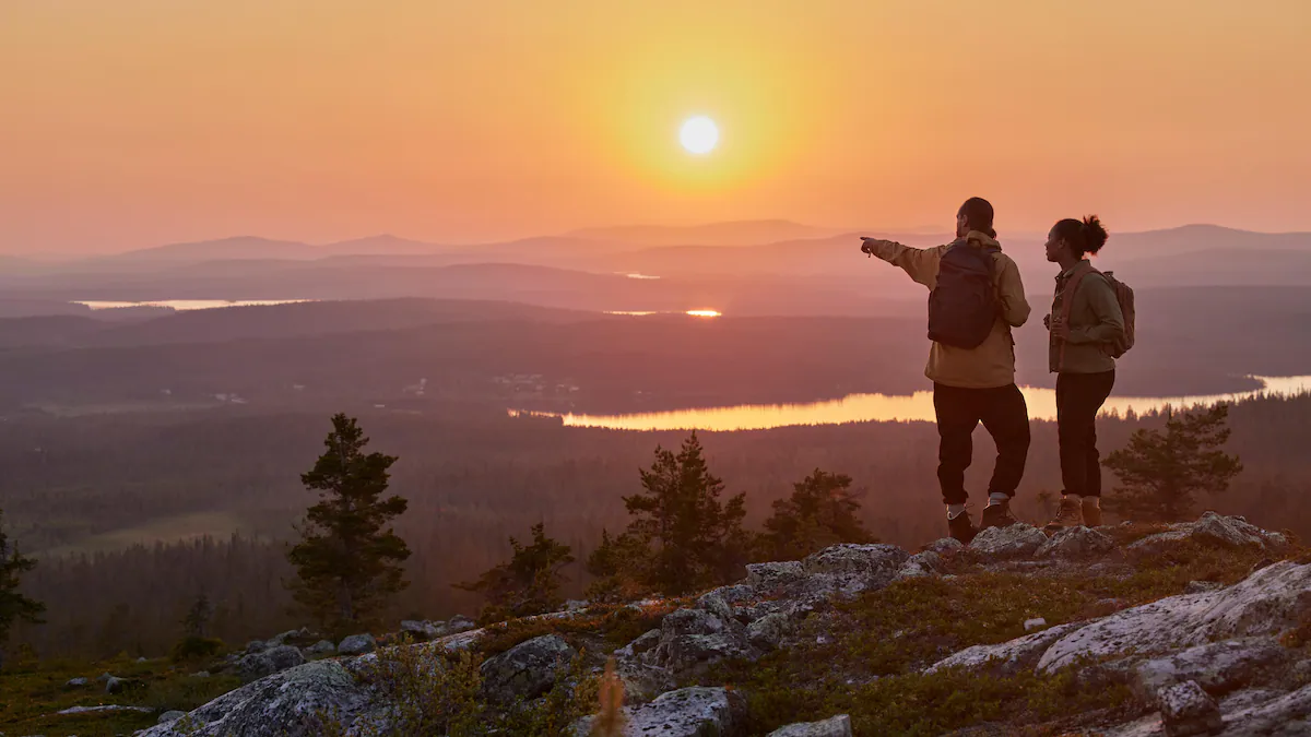 Two hikers admire the sunset over Lapland’s autumn landscape