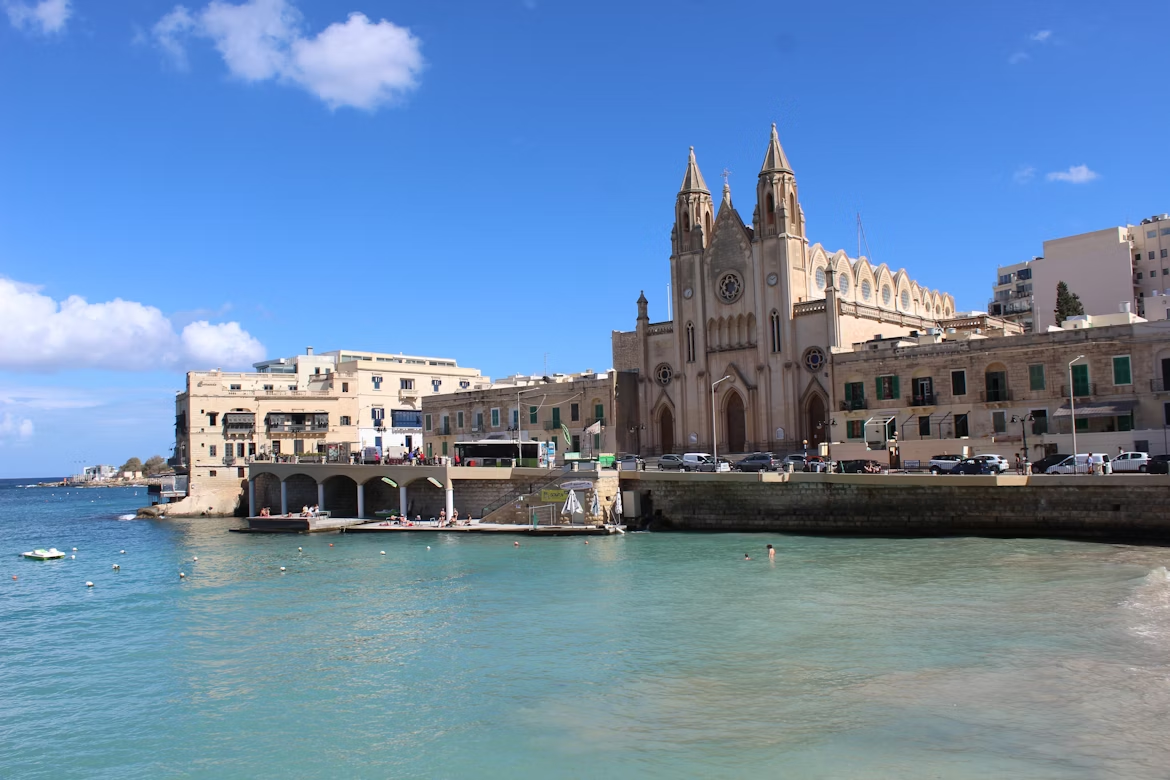 Scenic view of Balluta Bay with historic church and waterfront buildings in St Julian’s, Malta