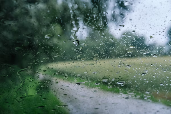 Raindrops on a window with a blurred rural path in the background