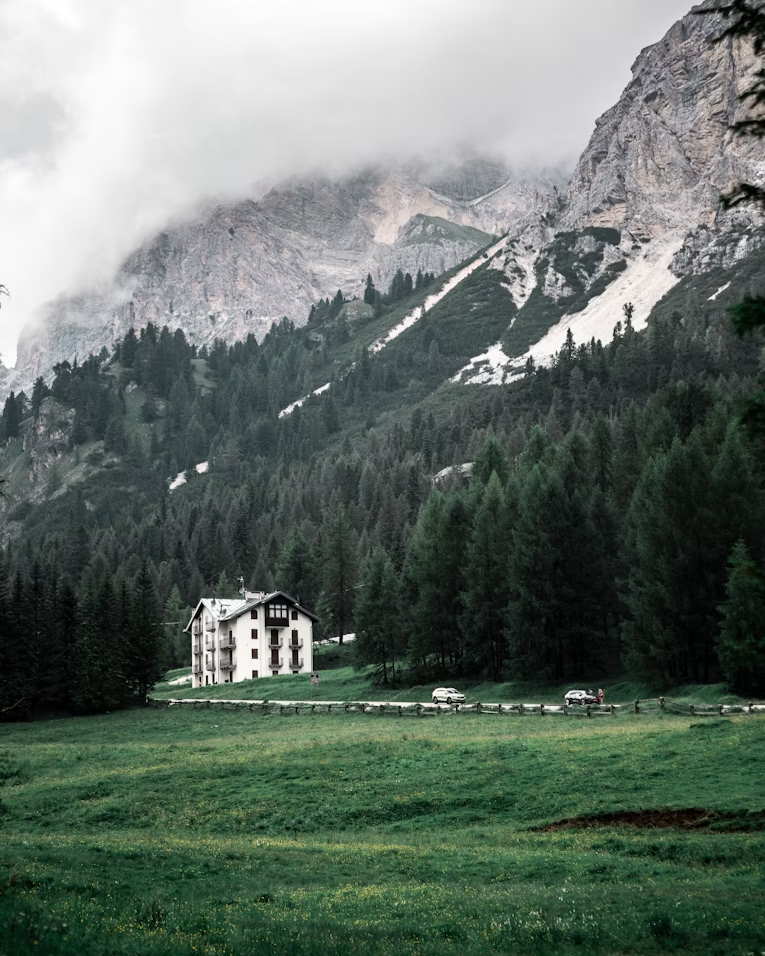 A solitary alpine hotel near a dense forest and dramatic mountain cliffs in Cortina d’Ampezzo under cloudy skies