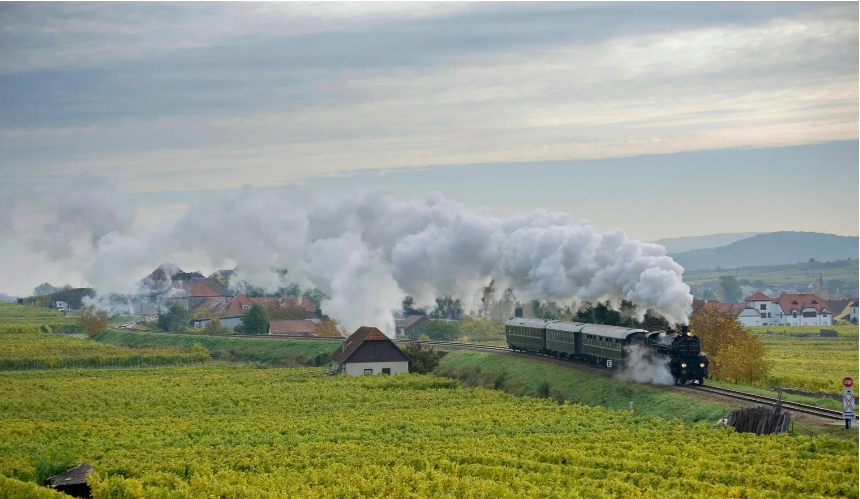 Steam train passing through vineyards near a European village