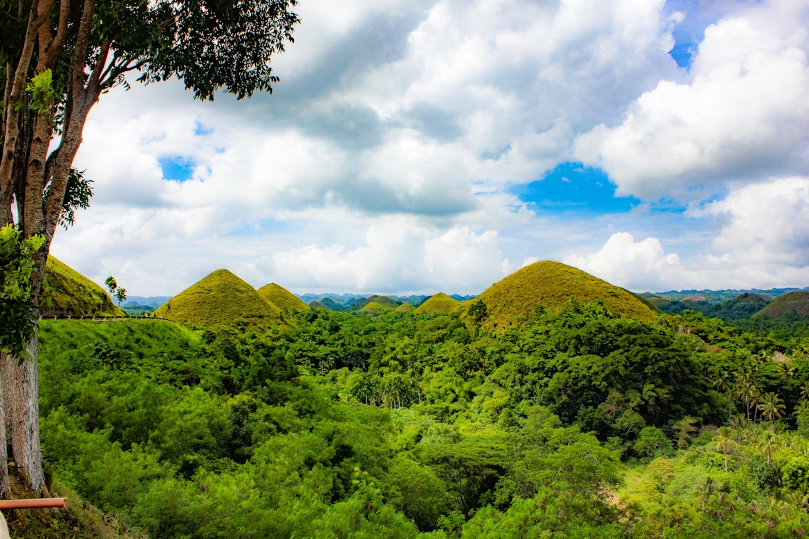 Scenic view of the Chocolate Hills surrounded by lush green forest under a partly cloudy sky