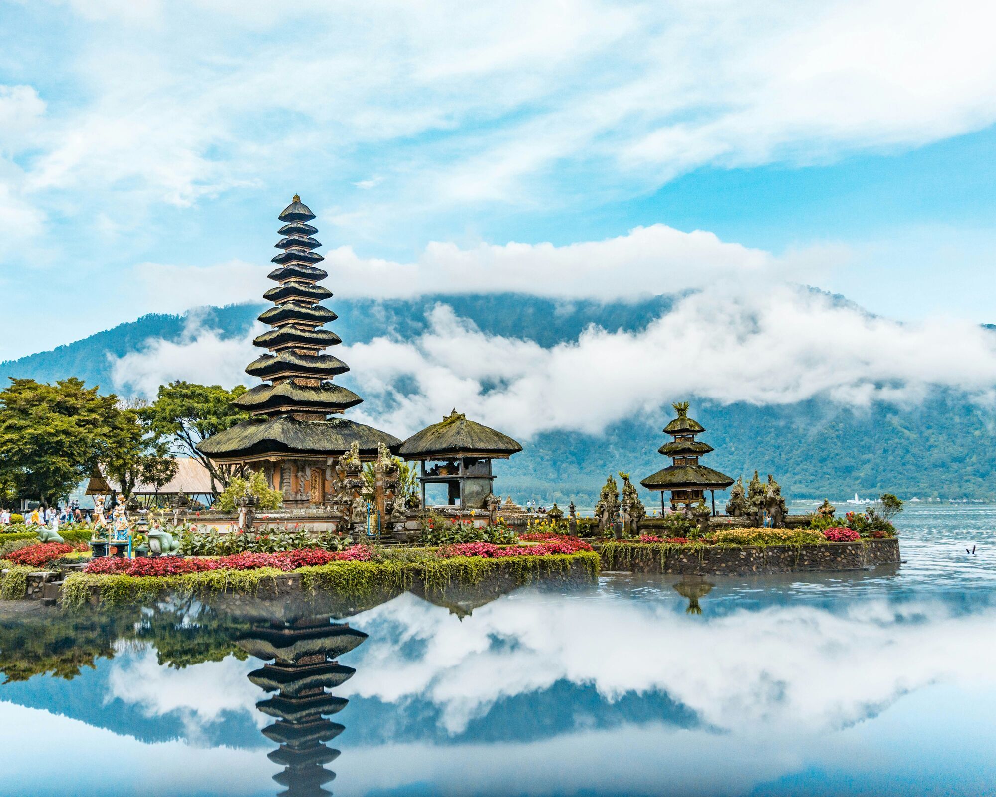 Balinese temple complex on a lakeside with mountains and clouds in the background