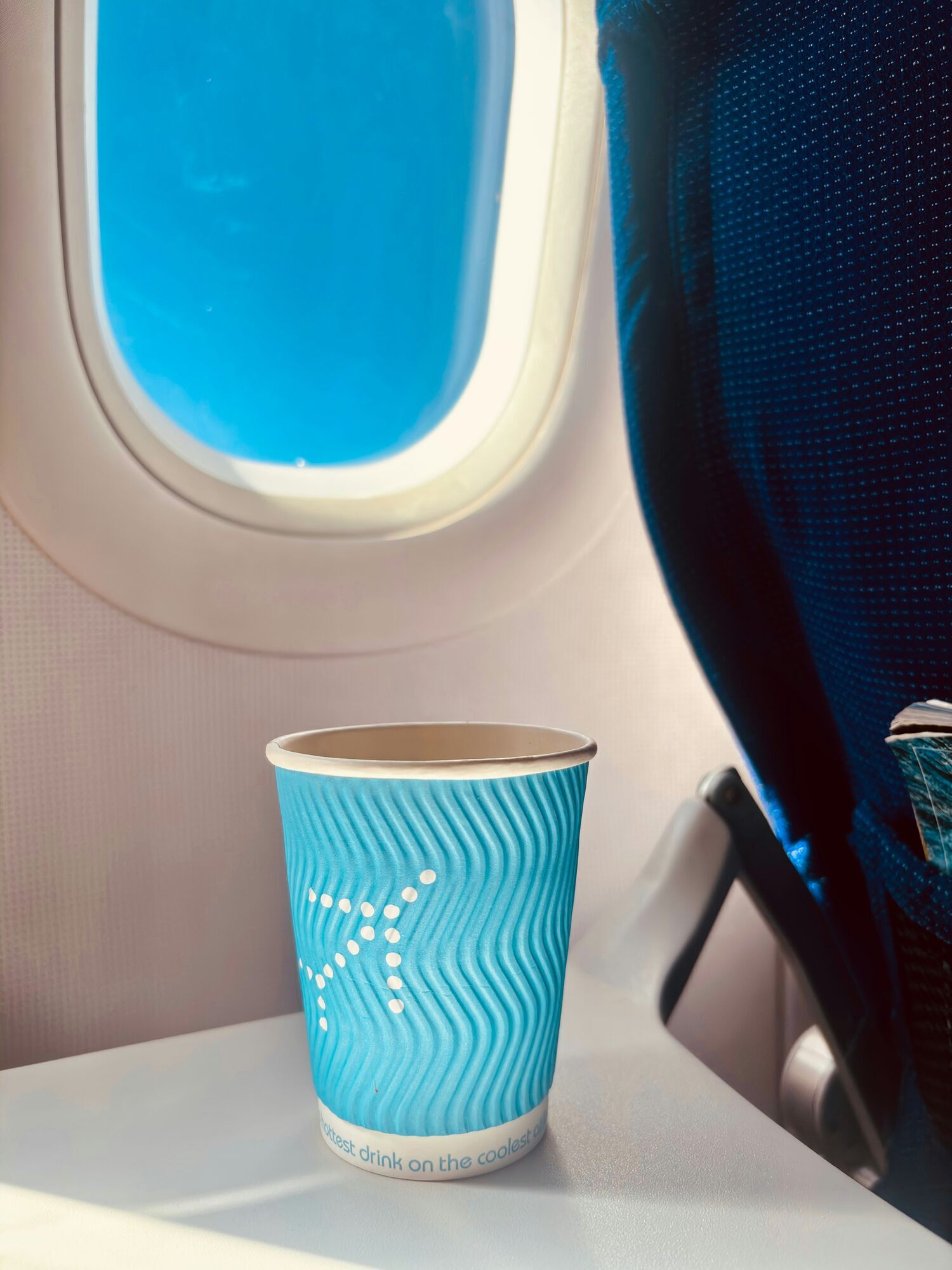 Paper cup placed on a tray table beside an aircraft window in flight