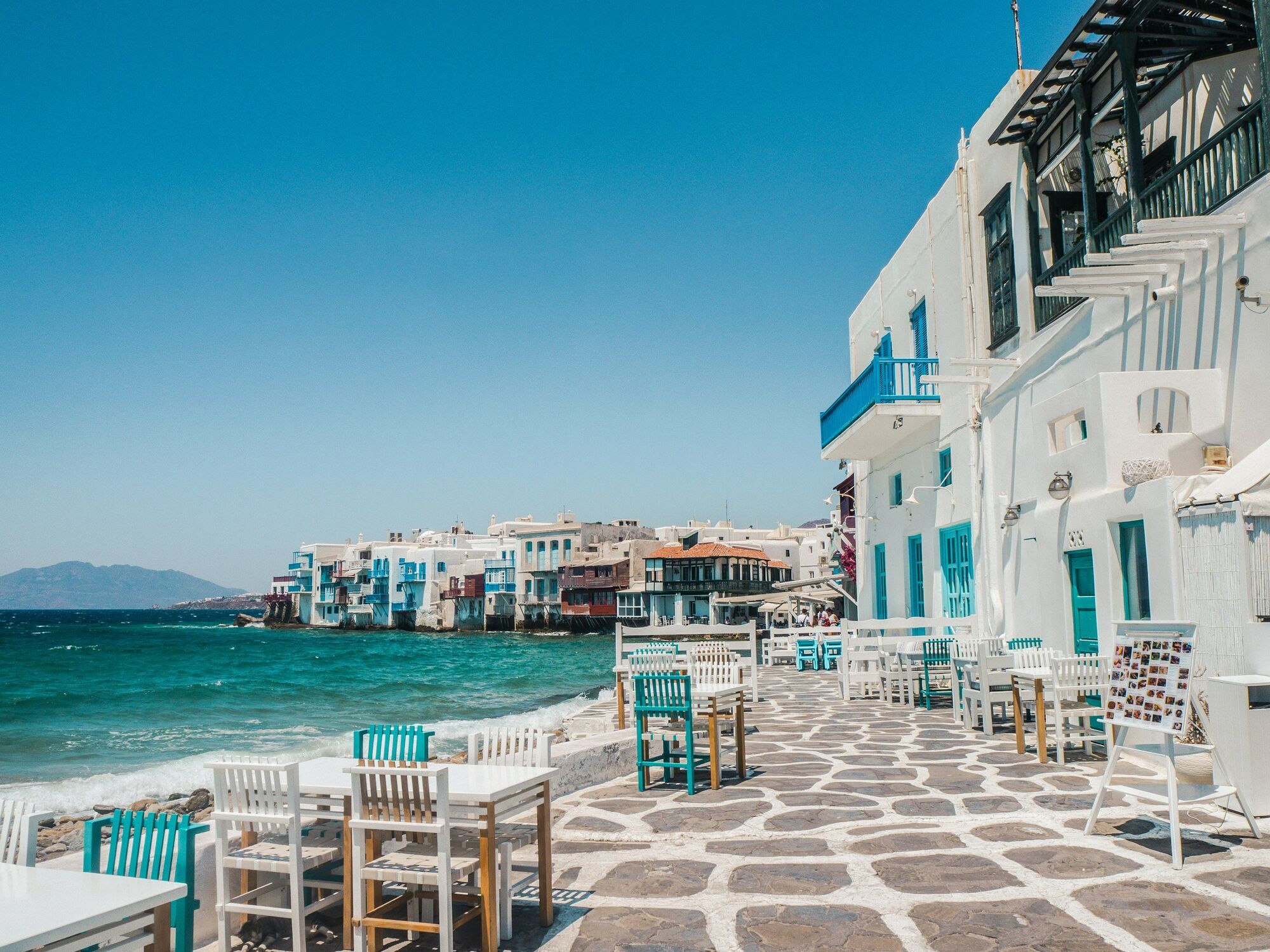 Seaside walkway in Mykonos with whitewashed houses and blue balconies along the water