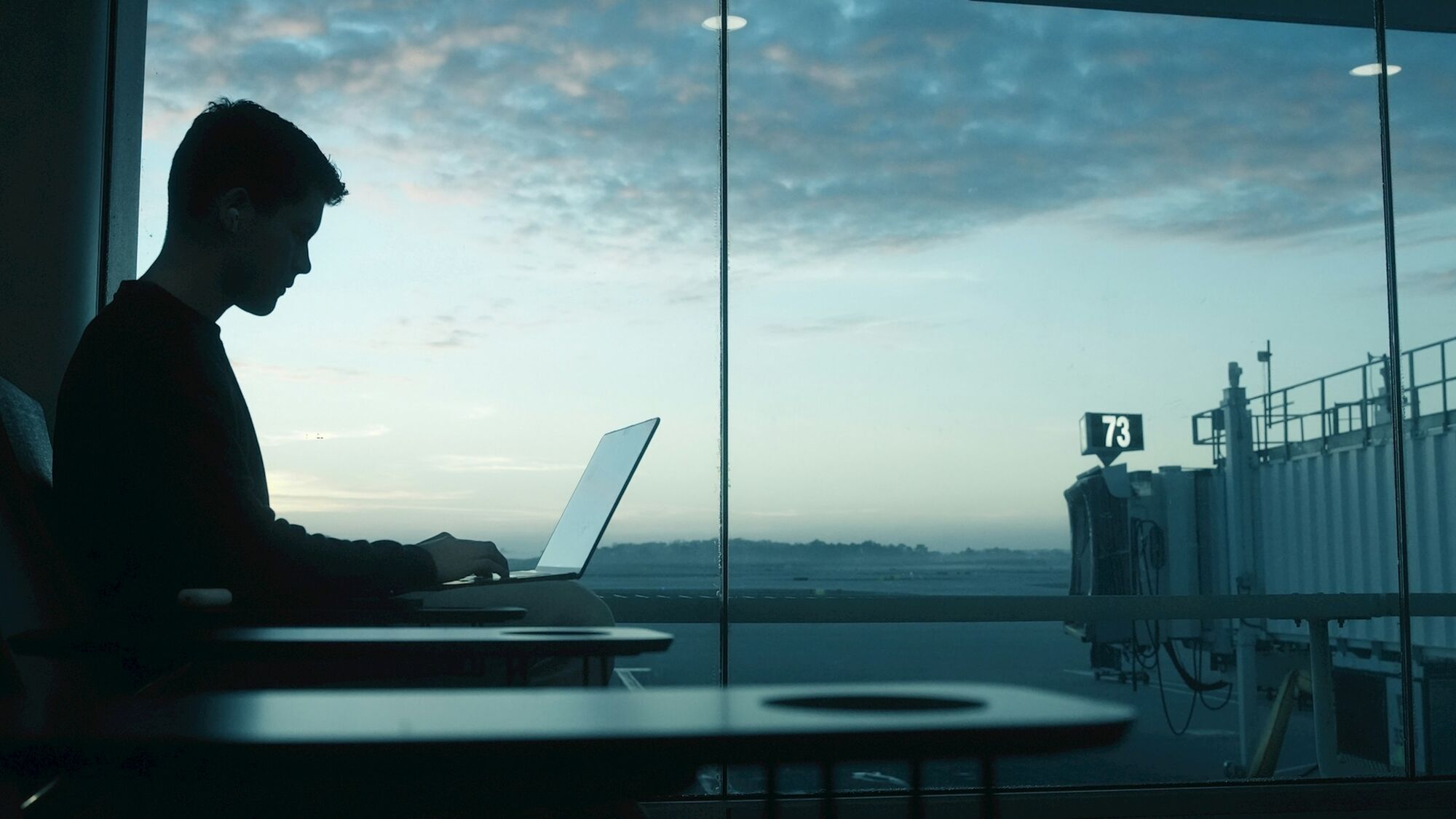 Traveller working on a laptop at an airport gate at dawn