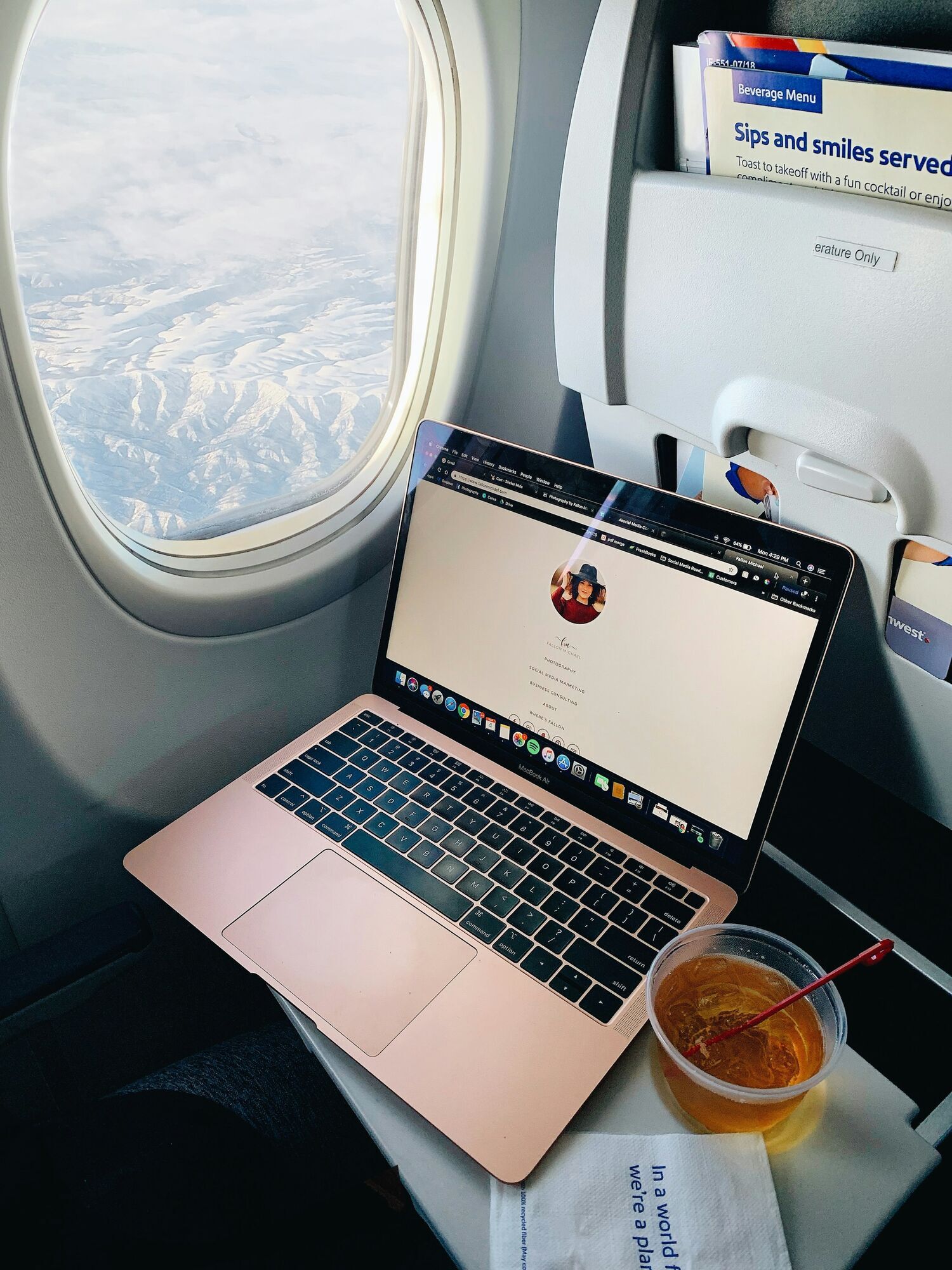 Laptop on tray table with drink near aircraft window