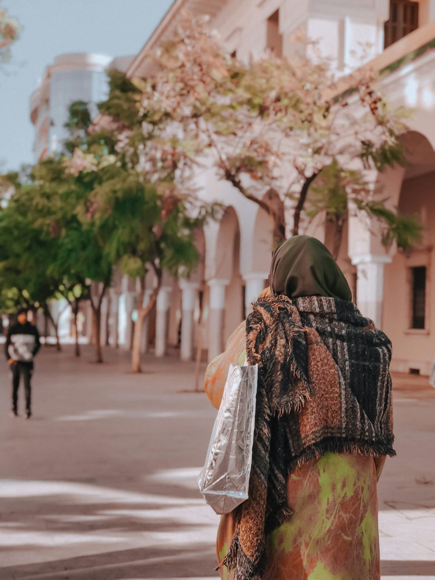 Pedestrian walking through a shaded street lined with trees in Oujda
