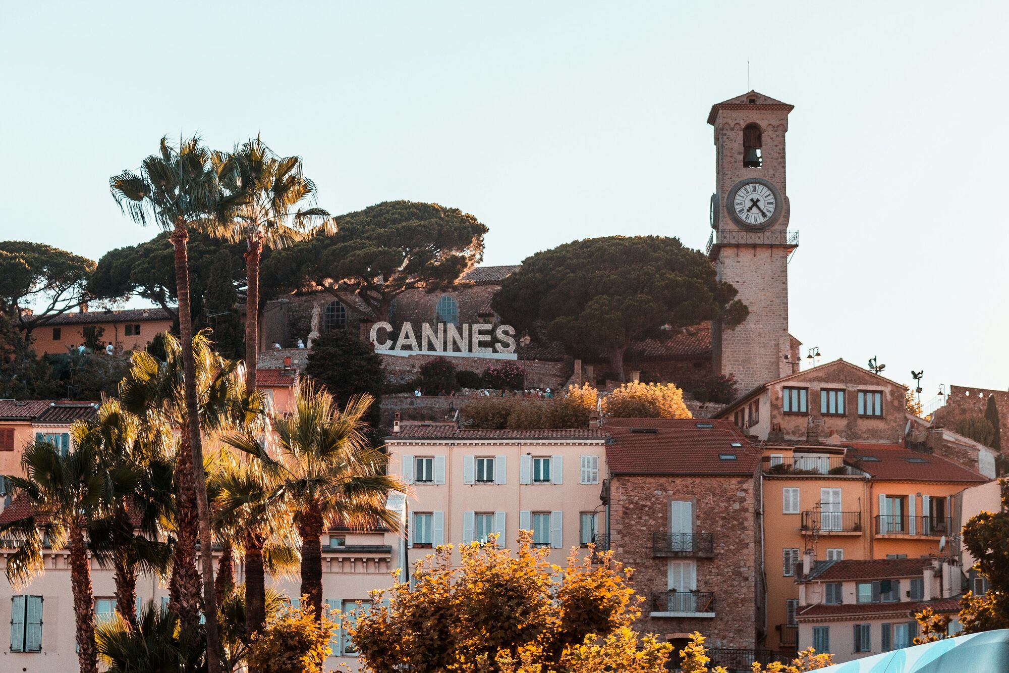 View of Cannes old town with clock tower and palm trees at golden hour