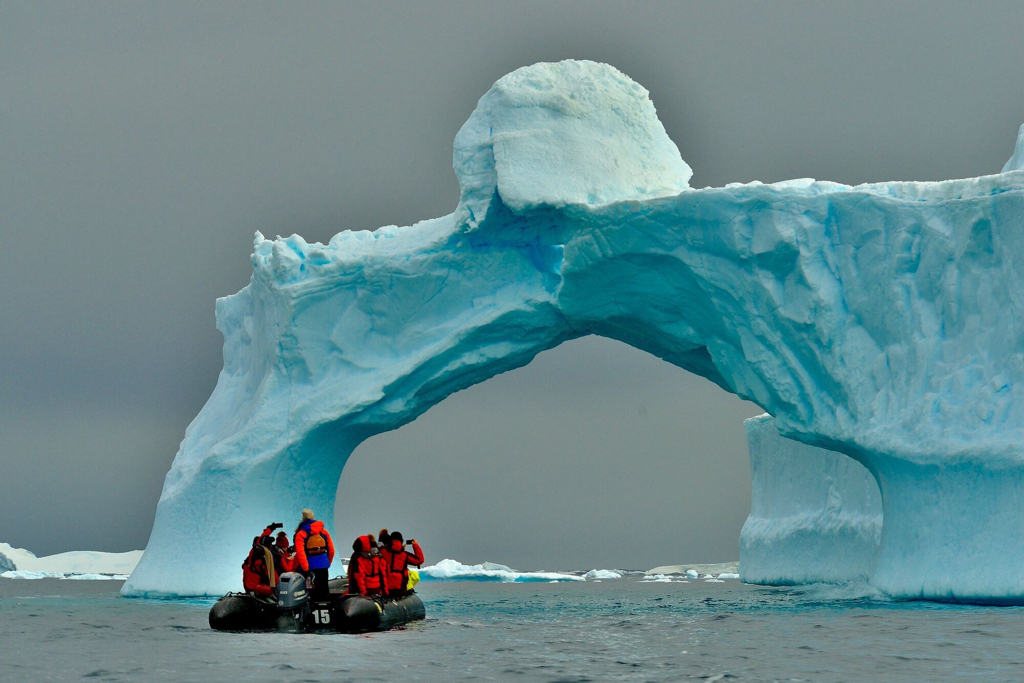 Tourists in Zodiac boat beside Antarctic ice arch