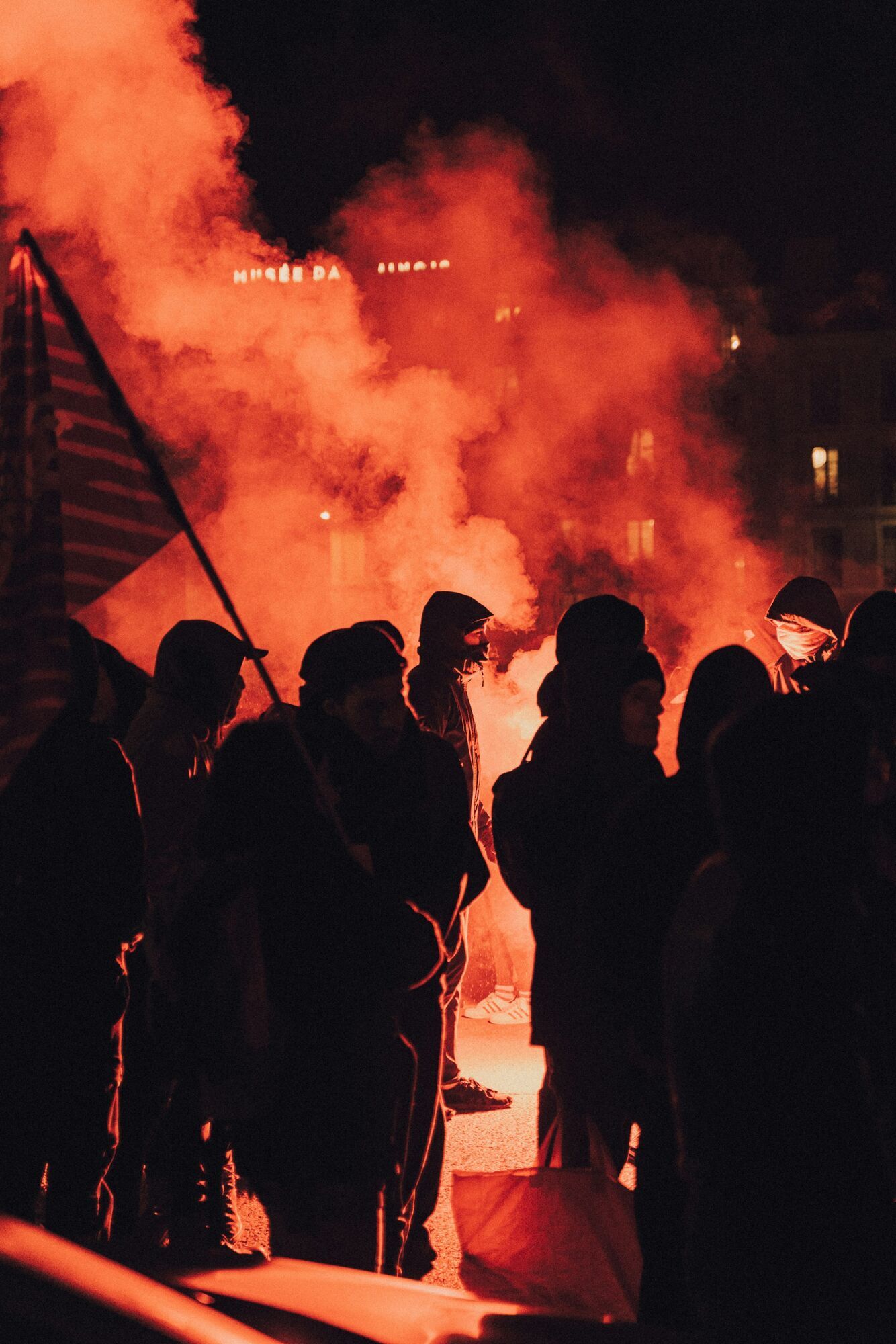 Hooded demonstrators silhouetted against red smoke