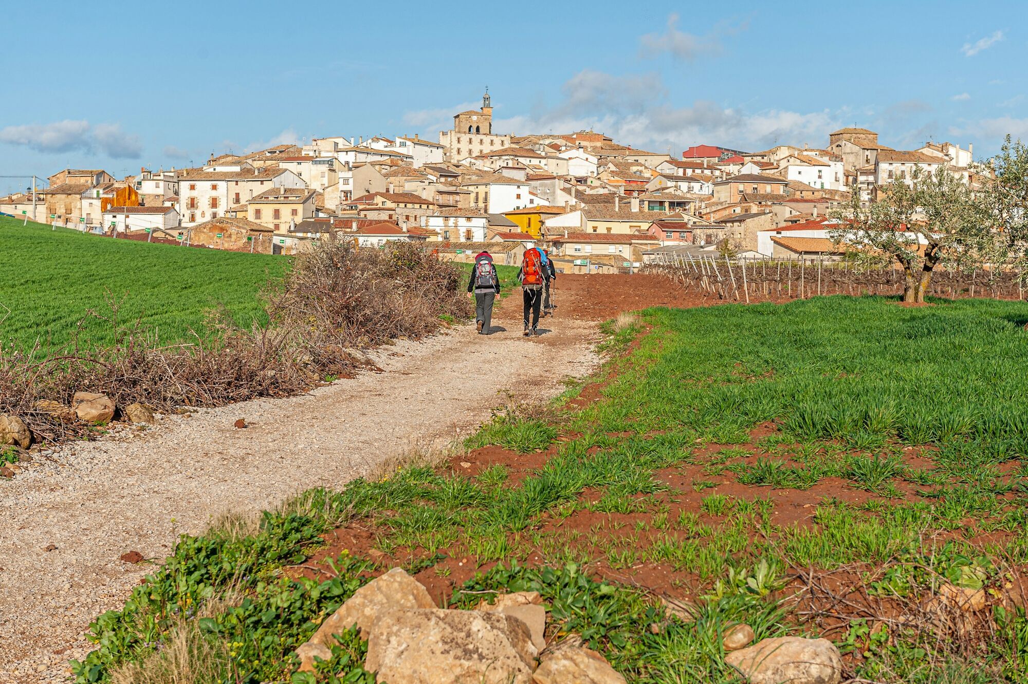 Two backpackers walking along a rural trail towards a Spanish town