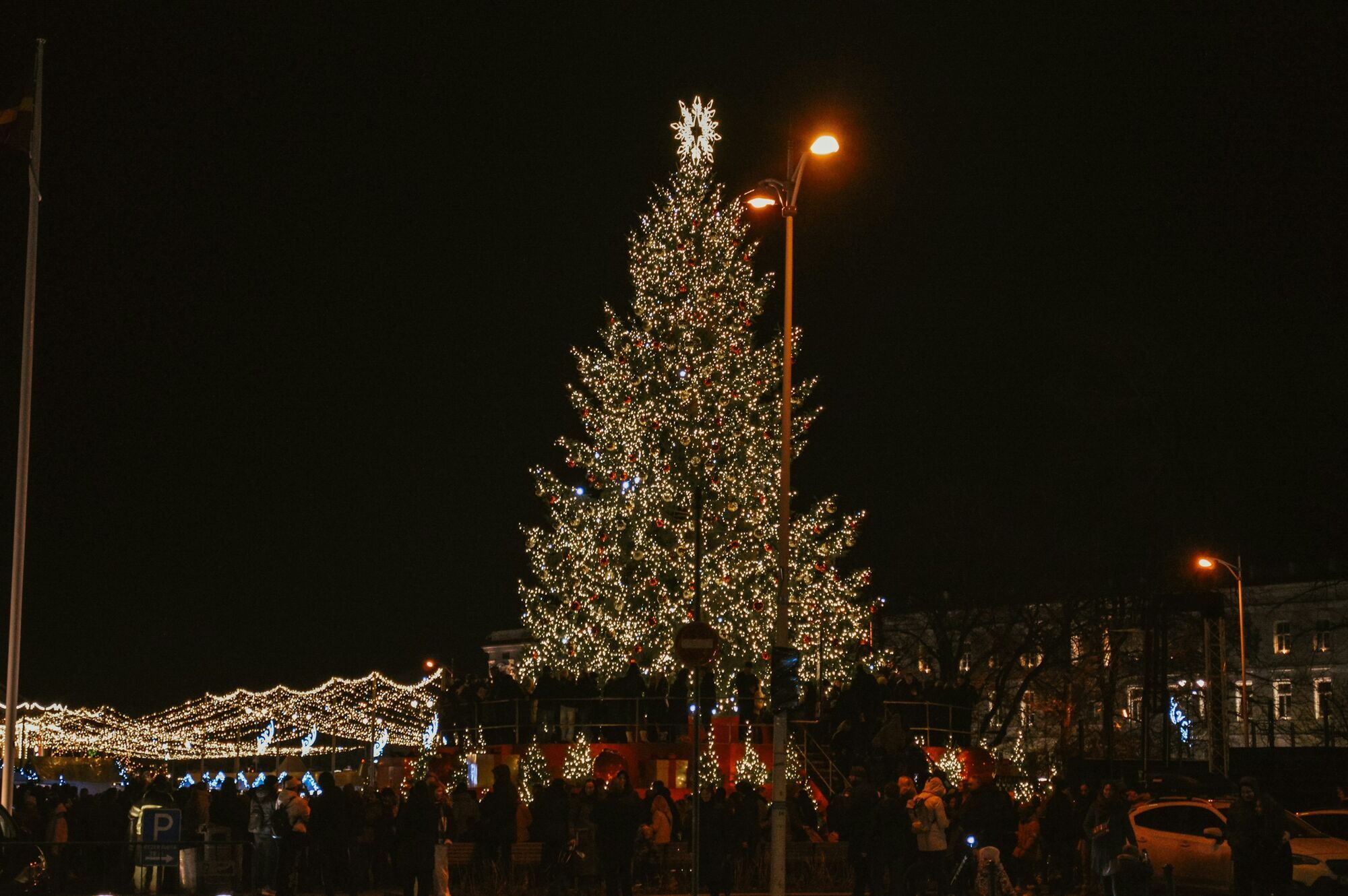 Large illuminated Christmas tree surrounded by people at night