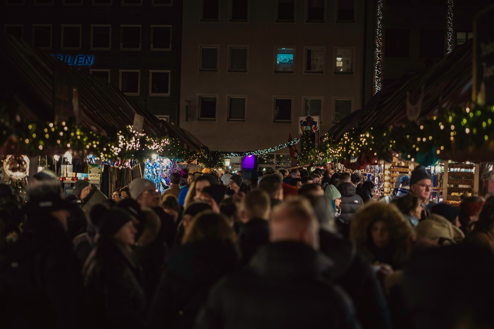 Crowds browsing illuminated Christmas market stalls at night