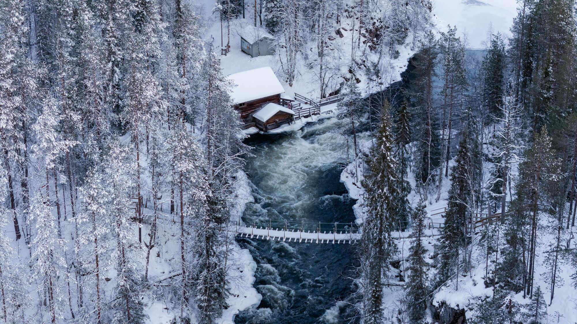 Snow-covered forest and wooden footbridge over a river in Kuusamo