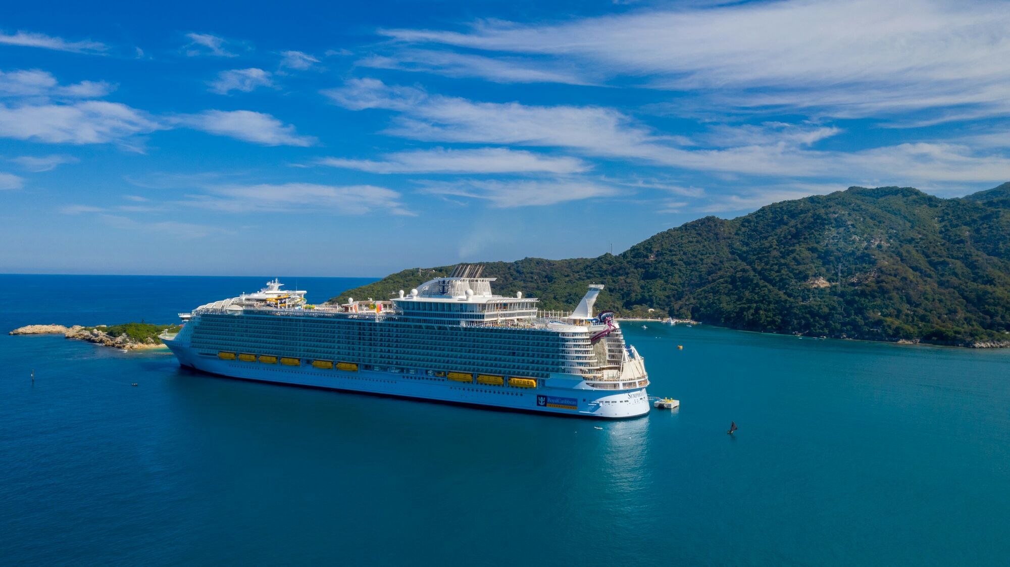 Royal Caribbean cruise ship in a bay beside green hills