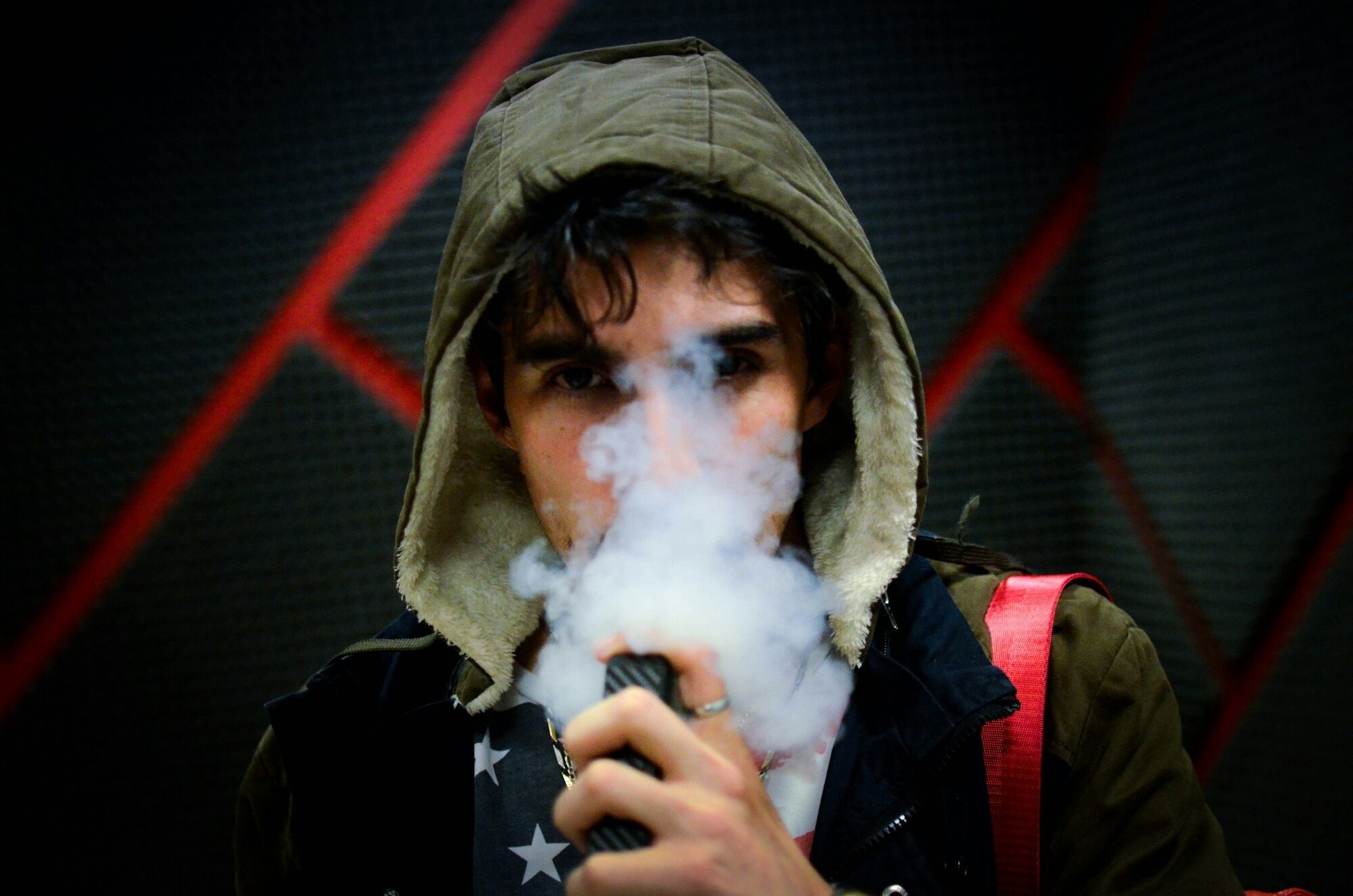 Man wearing a hooded jacket exhaling vapour from an electronic cigarette