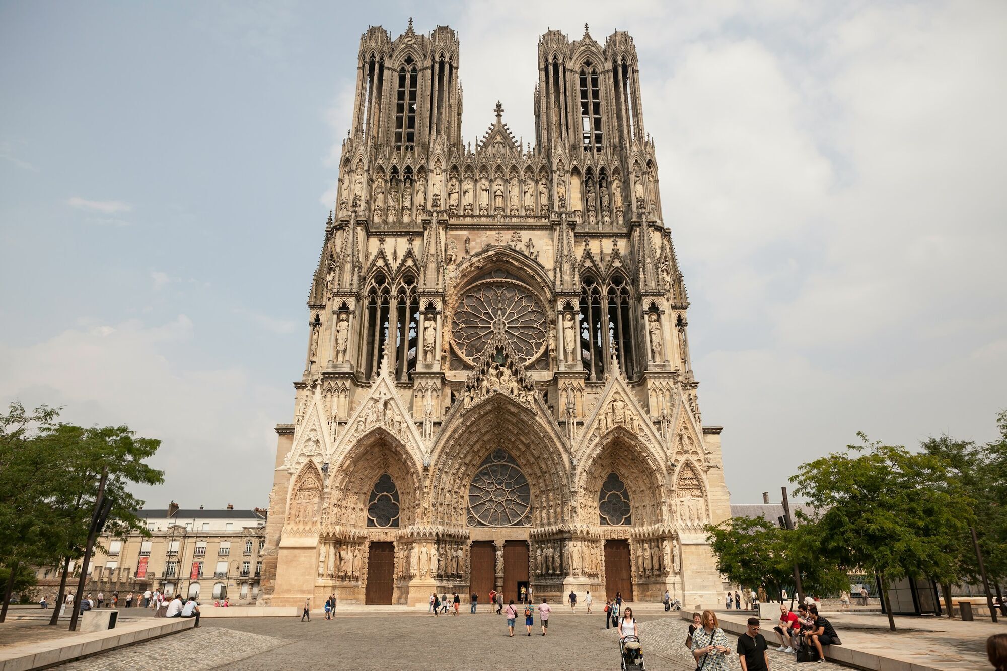 Gothic facade of Reims Cathedral in France with visitors in the square
