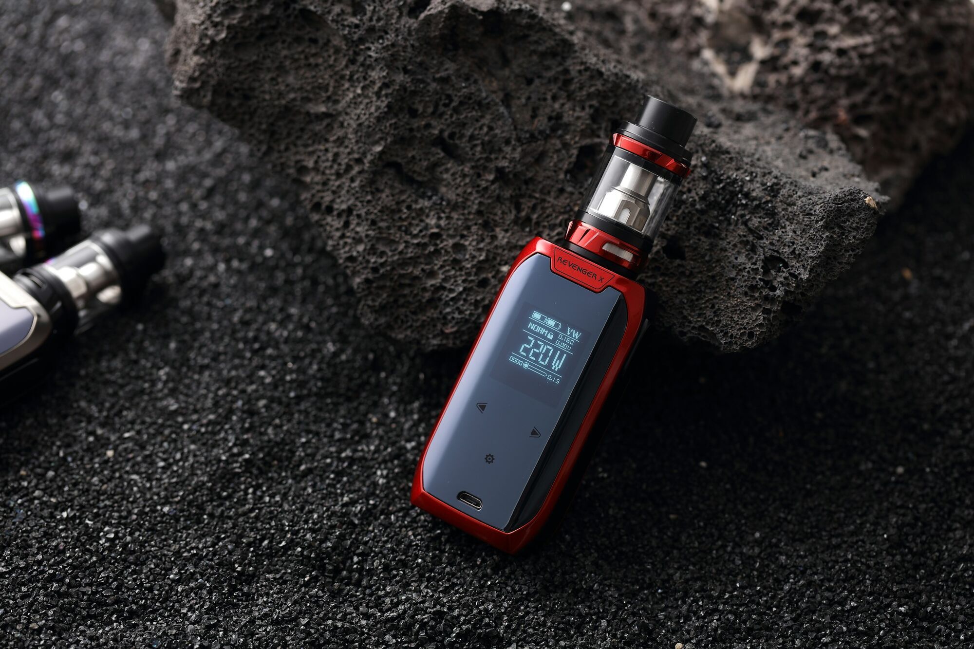 Red and black electronic vape device resting on a dark textured surface