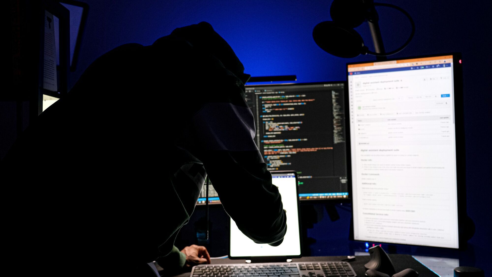 Hooded person working at several computer screens