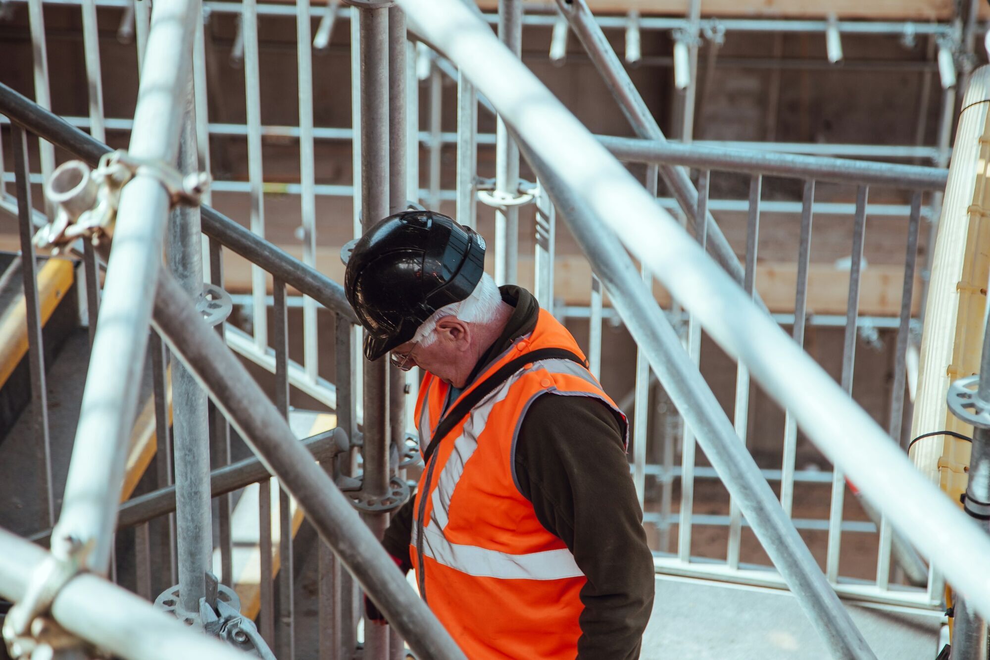Railway worker wearing an orange safety vest among metal scaffolding