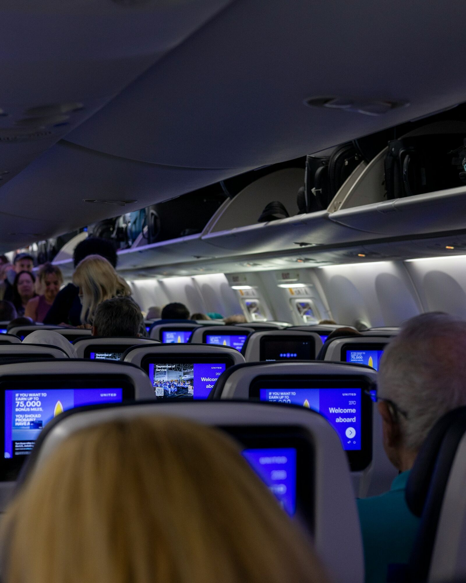 Passengers seated beneath aircraft overhead bins