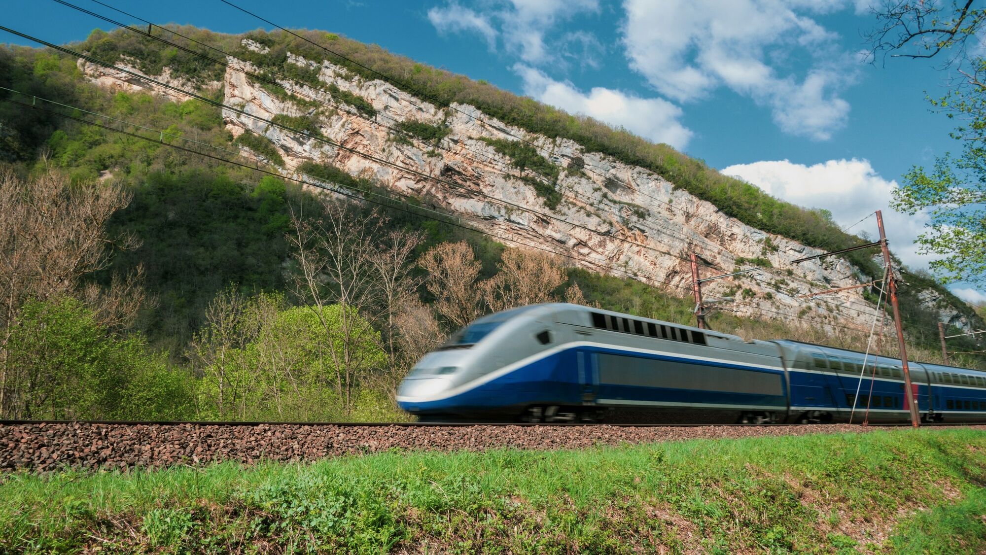 Passenger train travelling beneath rocky hills