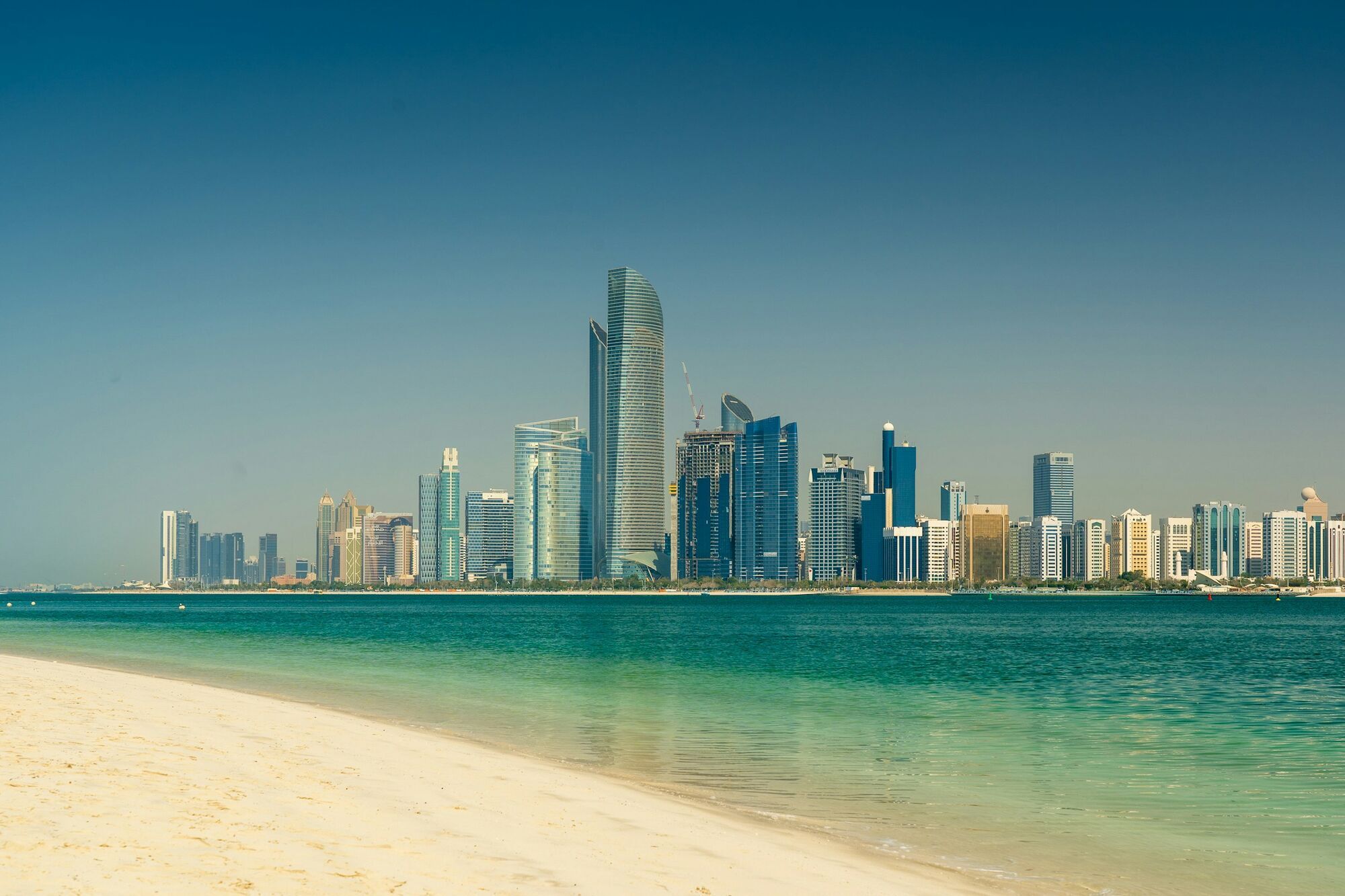 Abu Dhabi skyline viewed from sandy beach with turquoise water in the foreground