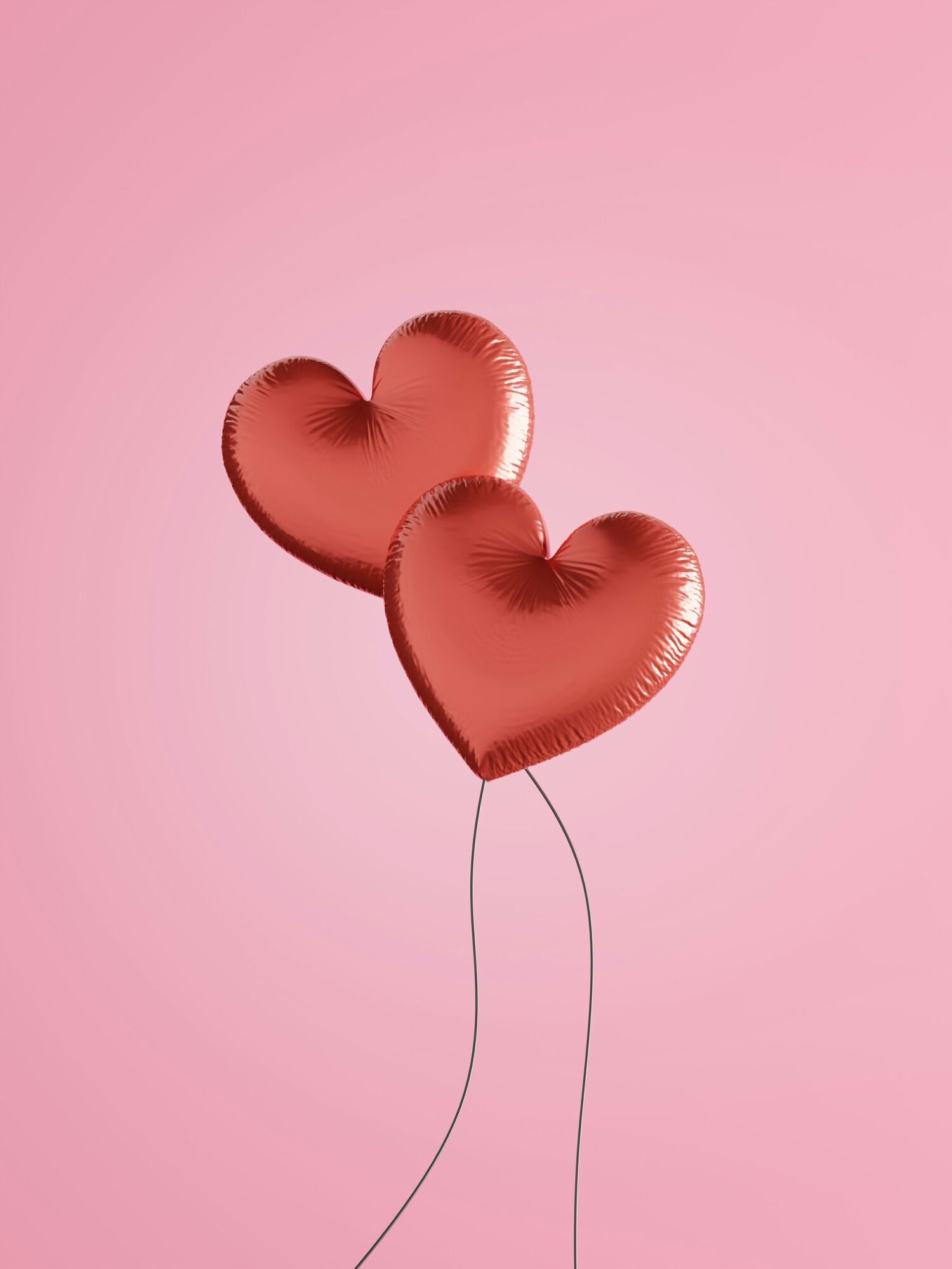 Heart-shaped balloons floating against a pink background