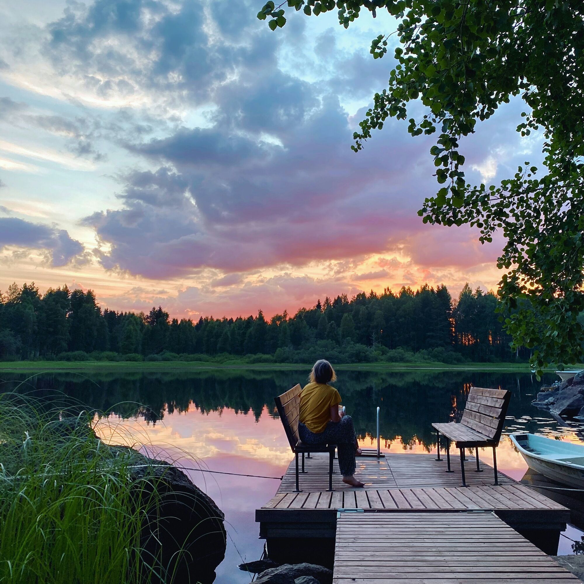 Person sitting on a wooden pier by a Finnish lake at sunset
