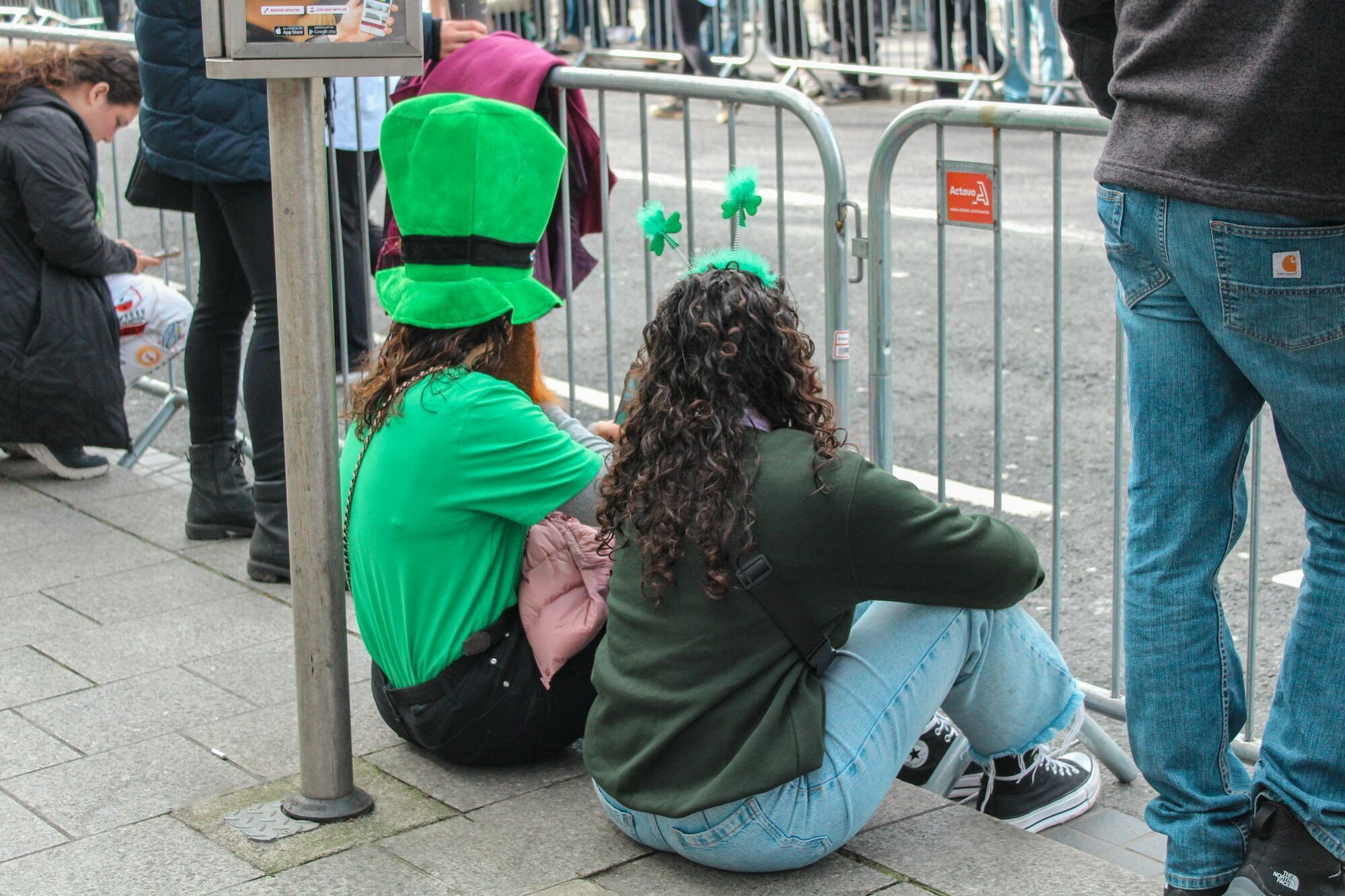 People in green outfits waiting behind barriers at St Patrick’s Day parade