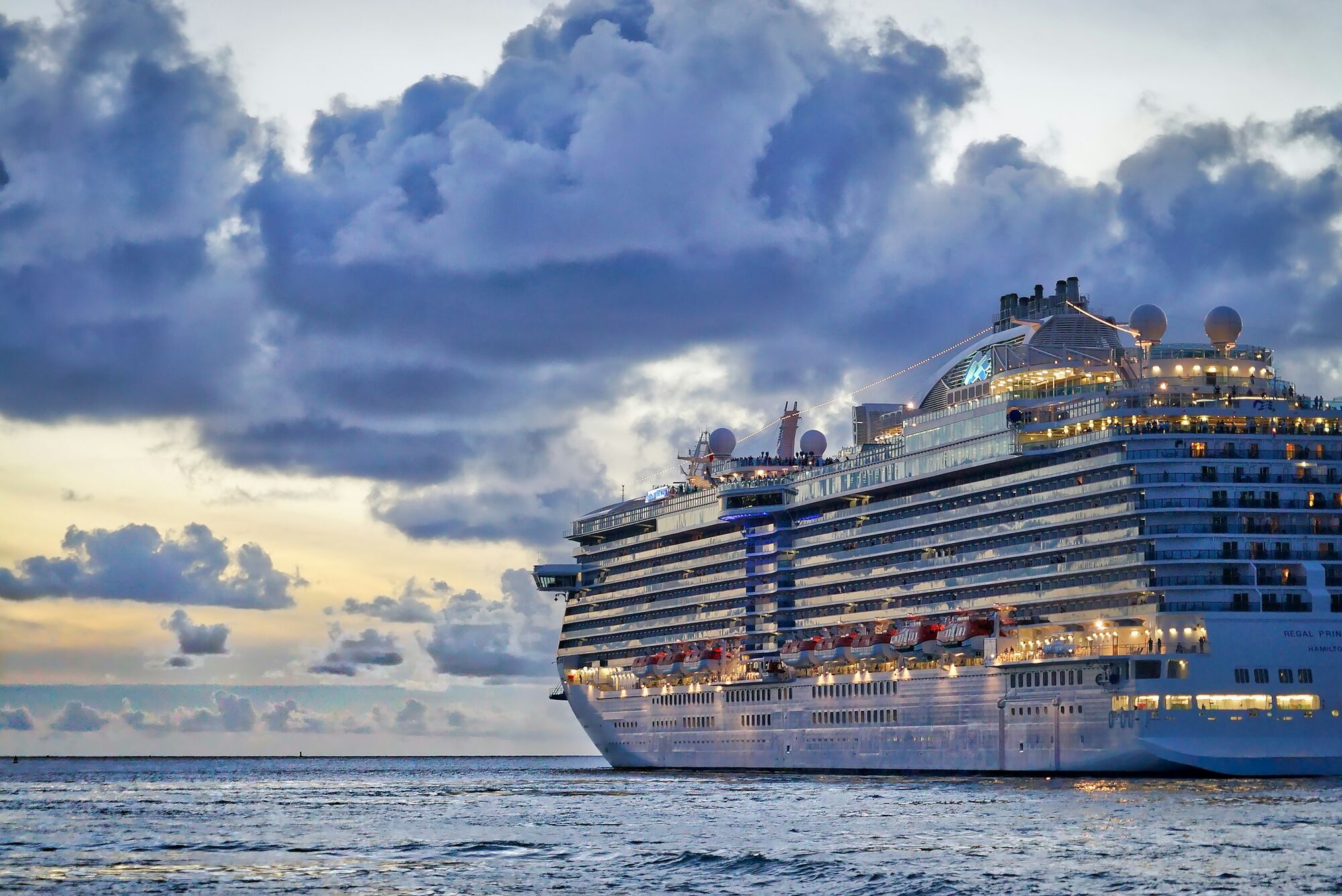 Large cruise ship sailing near coastline at dusk