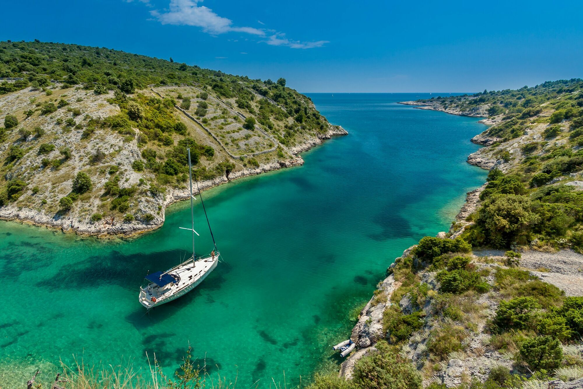 Turquoise coastal bay with yacht and rocky shoreline